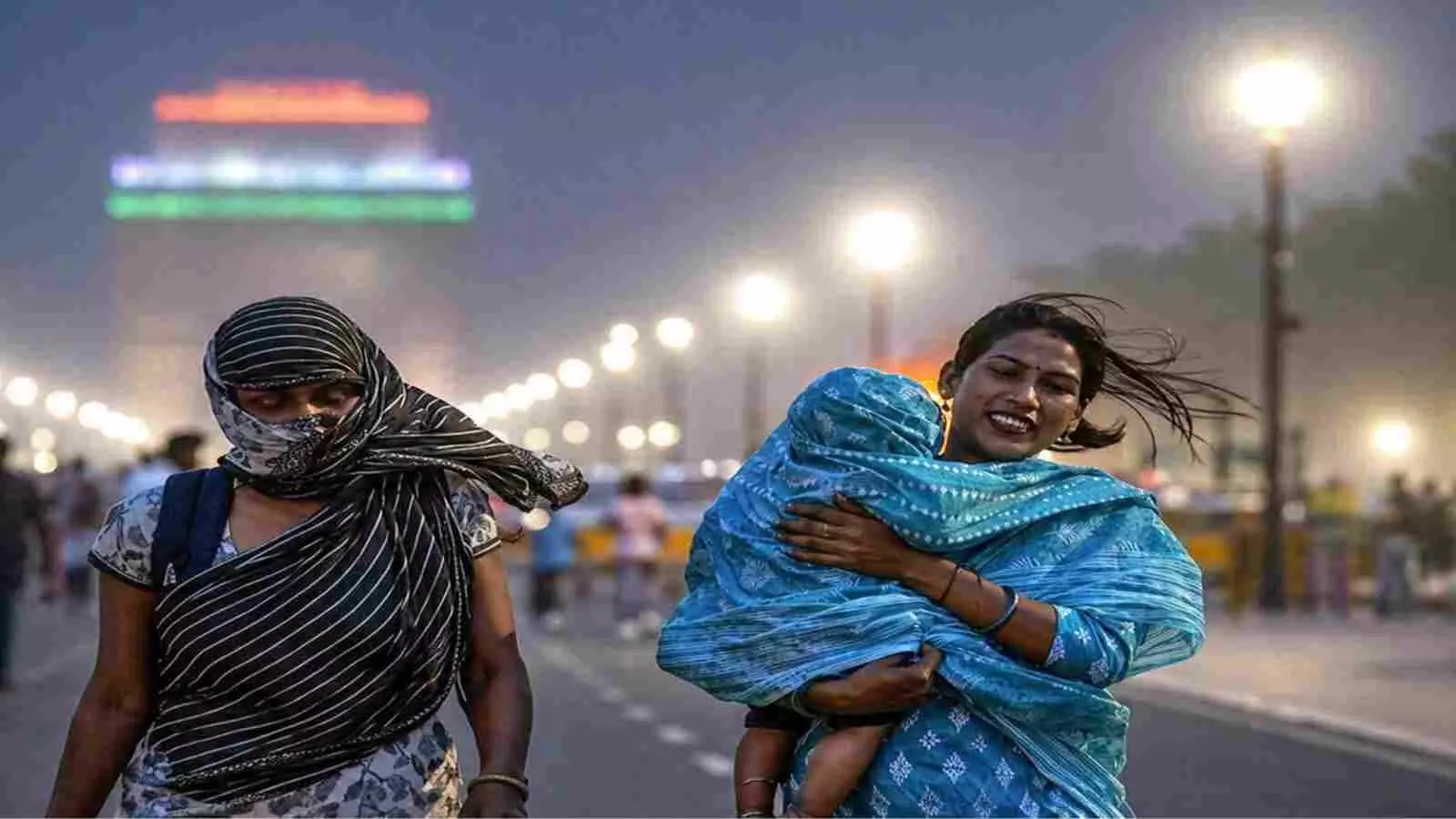 कर्तव्य पथ पर सिर ढके हुए पैदल चलती दो महिलाएं और धुंधला दिखाई देता इंडिया गेट।