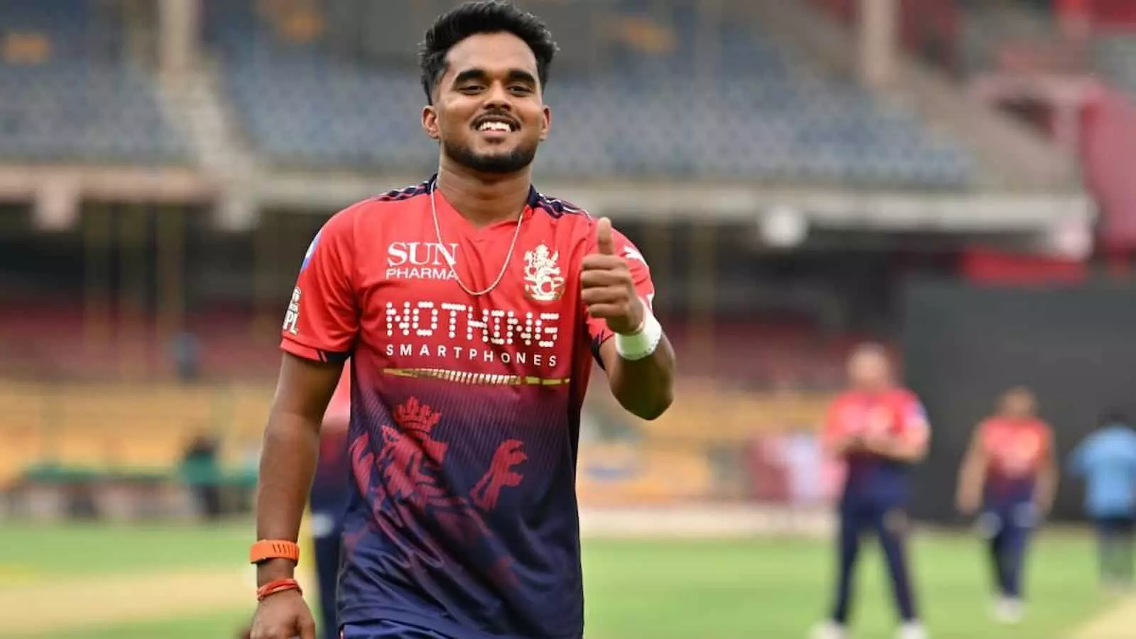 क्रिकेट स्टेडियम में आरसीबी की जर्सी पहने मुस्कराते हुए ऑलराउंडर मंगेश यादव का चित्र।