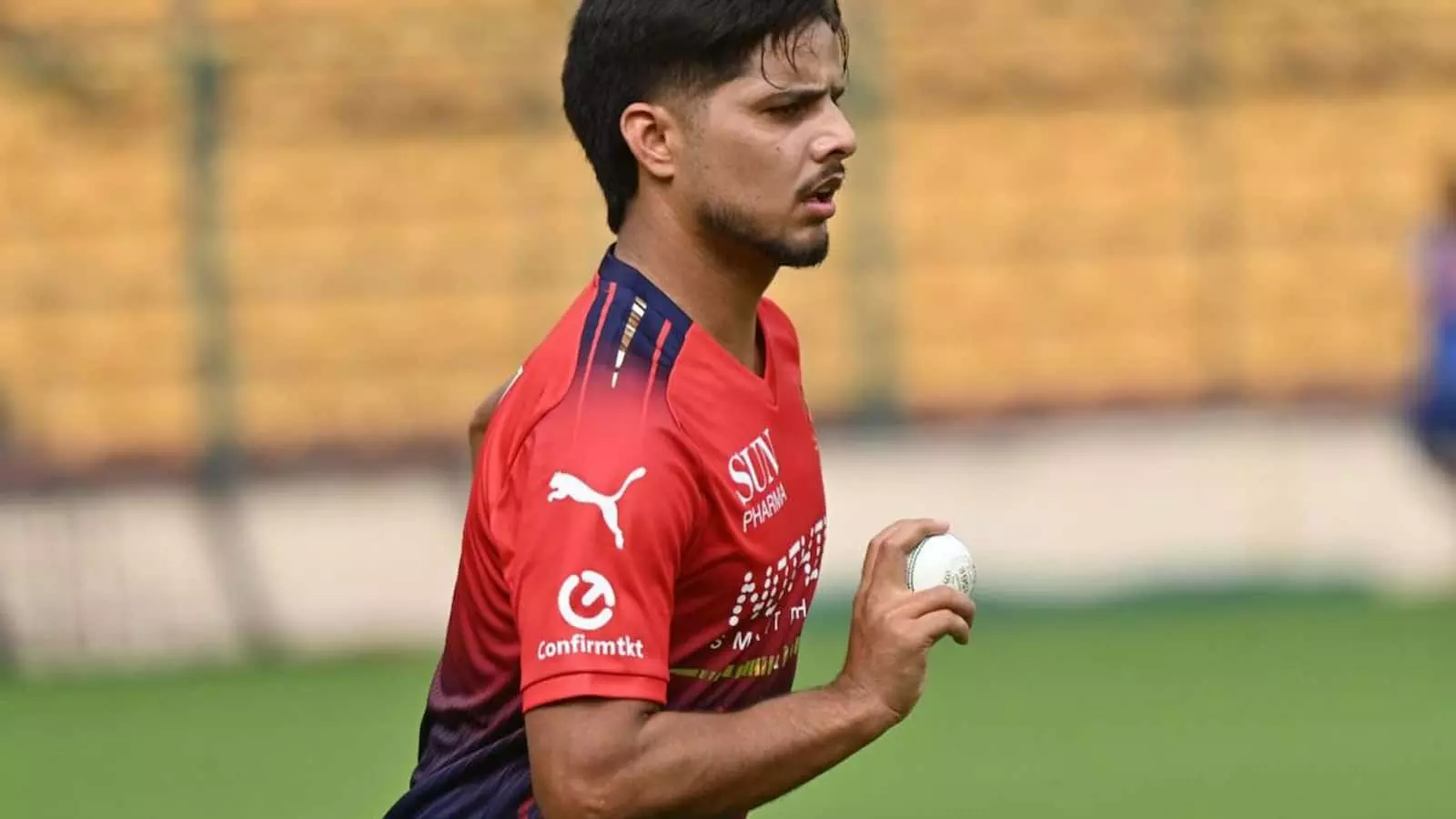 आरसीबी की जर्सी पहने तेज़ गेंदबाज़ रासिख सलाम डार क्रिकेट मैदान पर हाथ में गेंद लेकर दौड़ते हुए।
