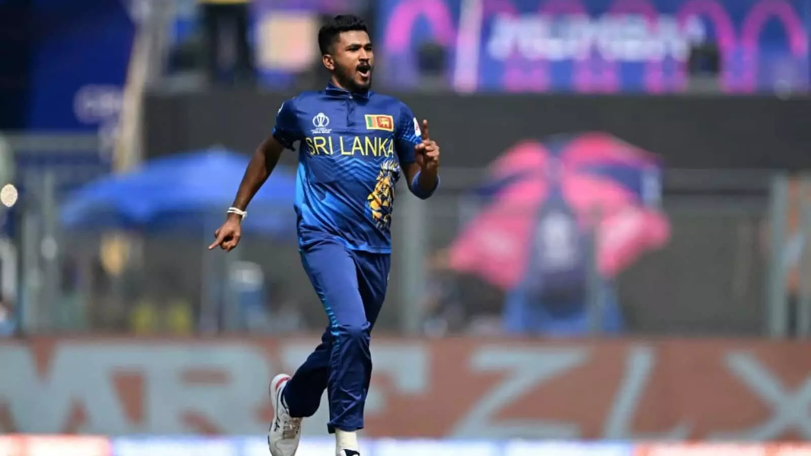 नीली जर्सी पहने श्रीलंकाई गेंदबाज़ दिलशान मदुशंका वानखेड़े स्टेडियम में विकेट लेने के बाद मैदान पर दौड़ते हुए। नीली जर्सी पहने श्रीलंकाई गेंदबाज़ दिलशान मदुशंका वानखेड़े स्टेडियम में विकेट लेने के बाद मैदान पर दौड़ते हुए।