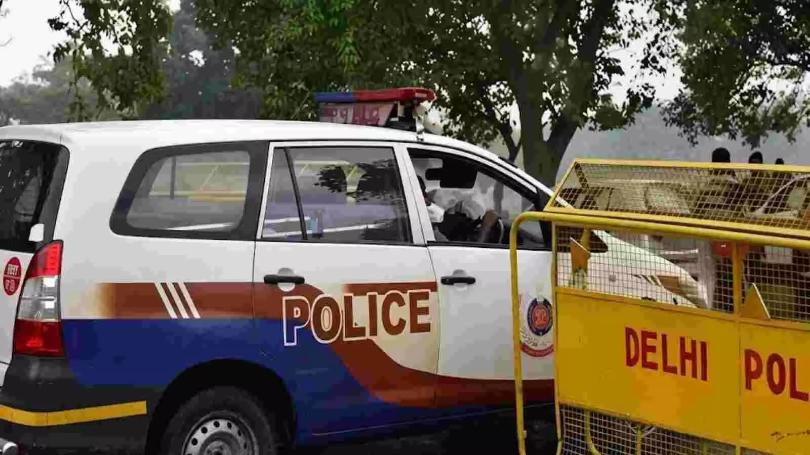सड़क किनारे खड़ी दिल्ली पुलिस की सफेद गाड़ी और पीला बैरिकेड राणा प्रताप बाग जांच के संदर्भ में दिख रहा है।
