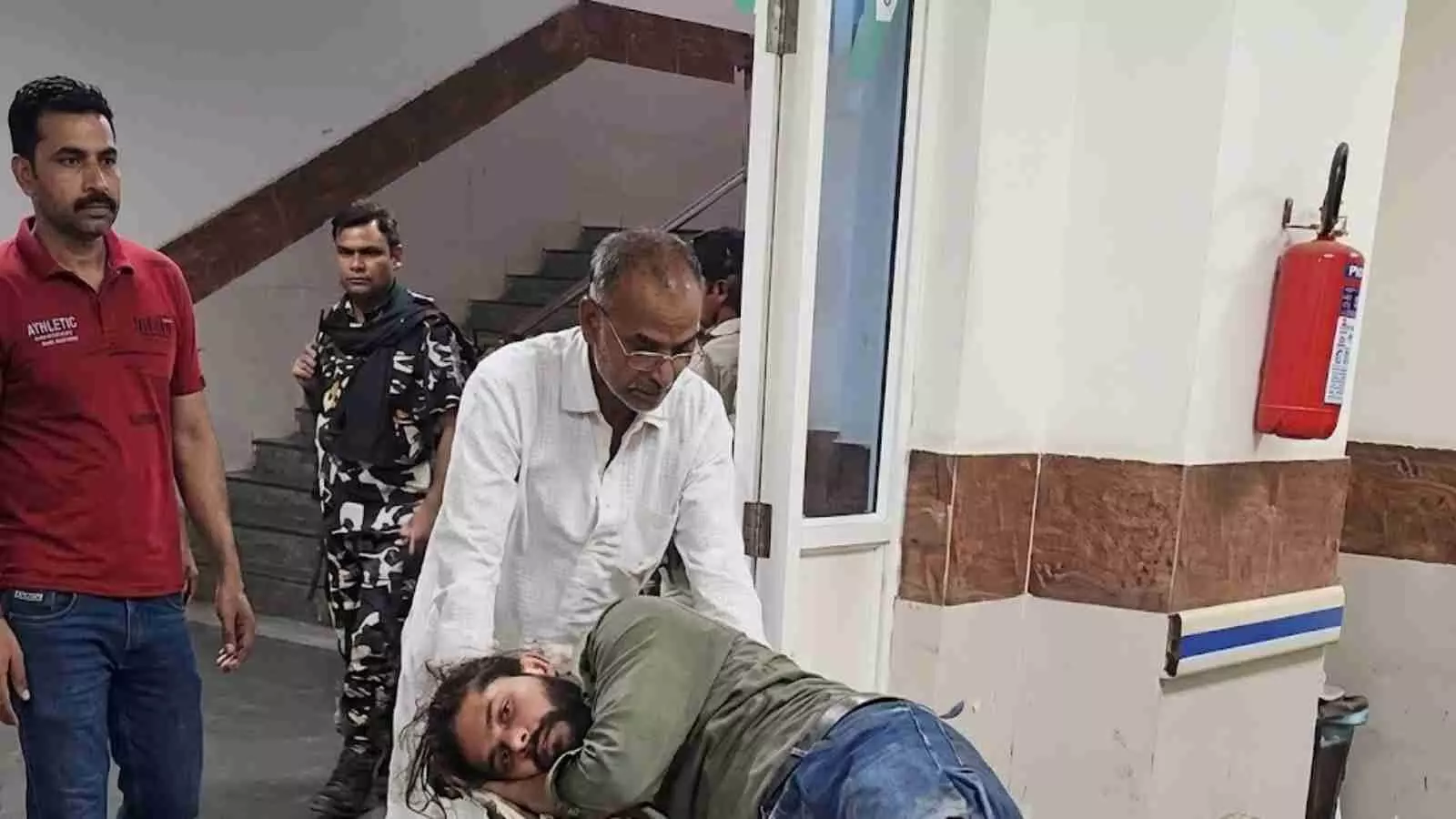 अस्पताल के स्ट्रेचर पर घायल व्यक्ति को ले जाते हुए स्वास्थ्यकर्मी और पुलिस अधिकारी।