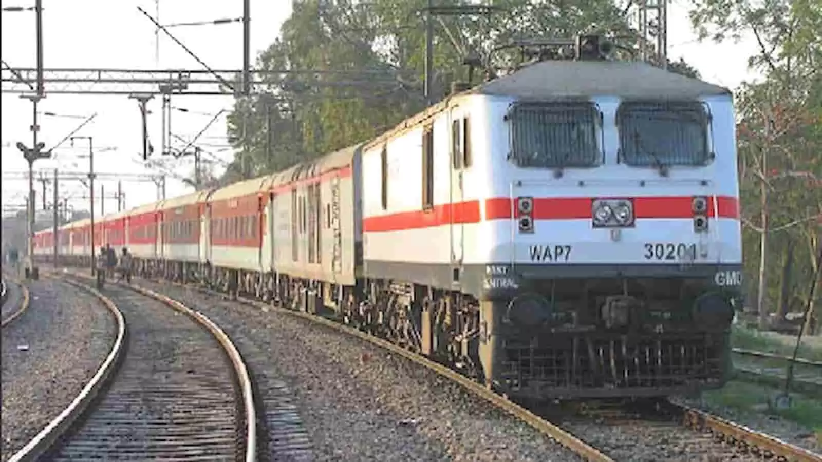 रेलवे ट्रैक पर चलती हुई सफेद और लाल रंग की एलएचबी कोच वाली एक्सप्रेस ट्रेन।