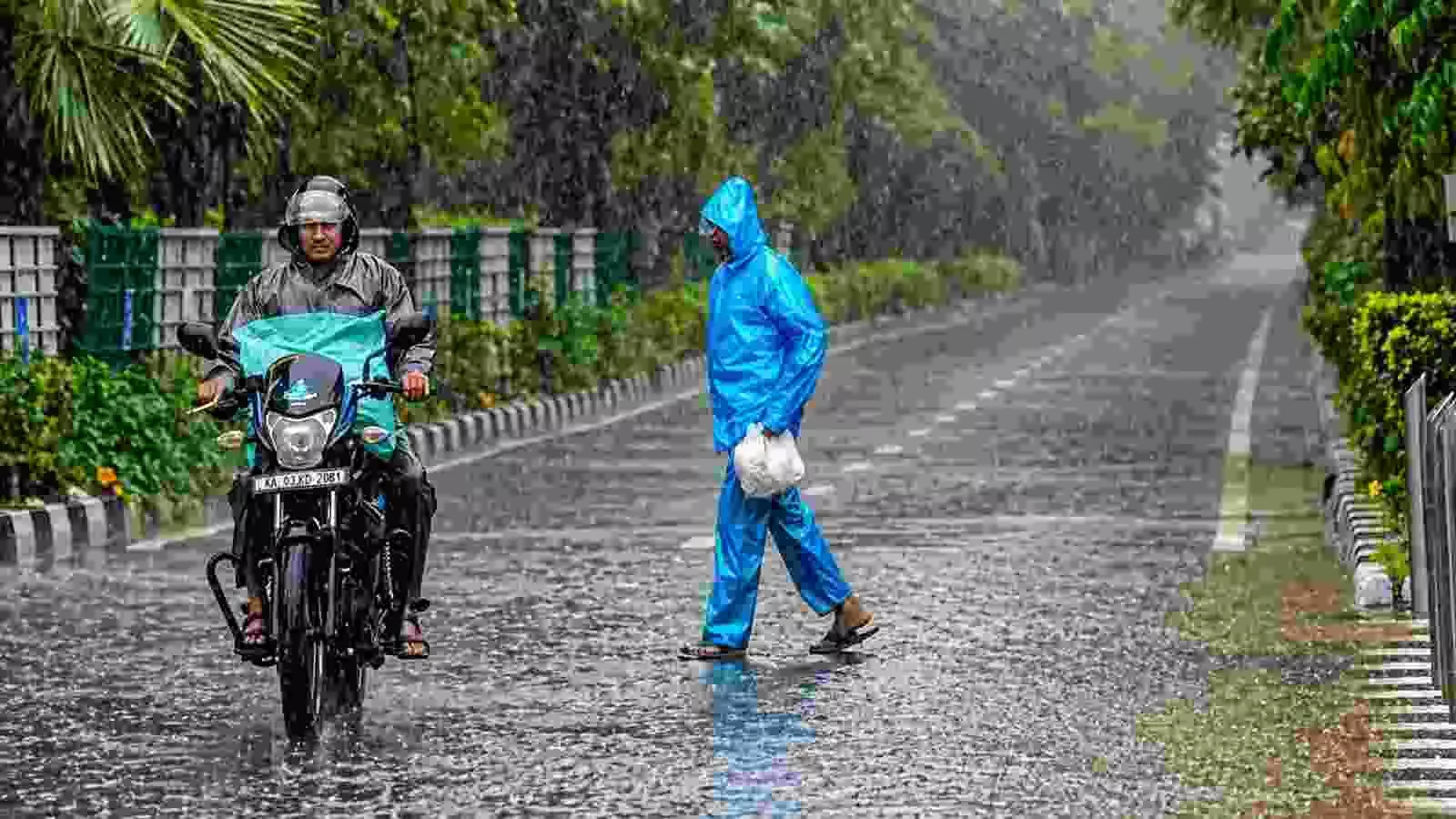 दिल्ली की सड़क पर बारिश के दौरान रेनकोट पहने व्यक्ति और मोटरसाइकिल सवार चलते हुए। दिल्ली की सड़क पर बारिश के दौरान रेनकोट पहने व्यक्ति और मोटरसाइकिल सवार चलते हुए।