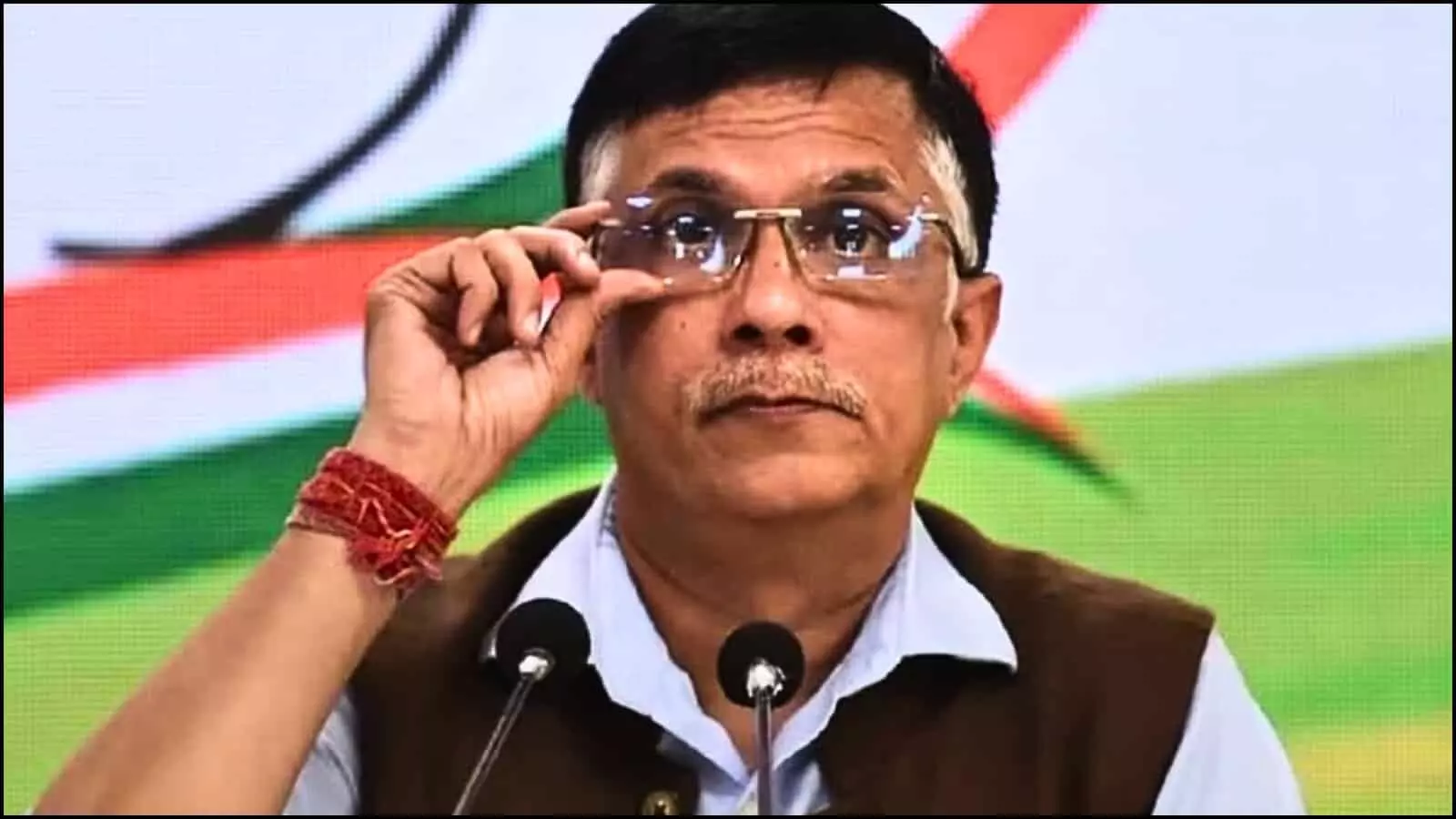चश्मा ठीक करते हुए पवन खेड़ा प्रेस कॉन्फ्रेंस के दौरान माइक के सामने गंभीर मुद्रा में दिख रहे हैं।