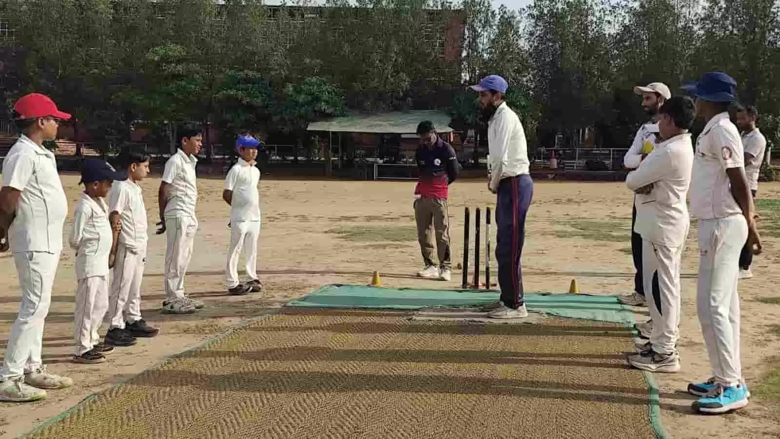 क्रिकेट पिच पर कोच से प्रशिक्षण लेते सफेद जर्सी पहने युवा खिलाड़ी और सहायक स्टाफ। क्रिकेट पिच पर कोच से प्रशिक्षण लेते सफेद जर्सी पहने युवा खिलाड़ी और सहायक स्टाफ।