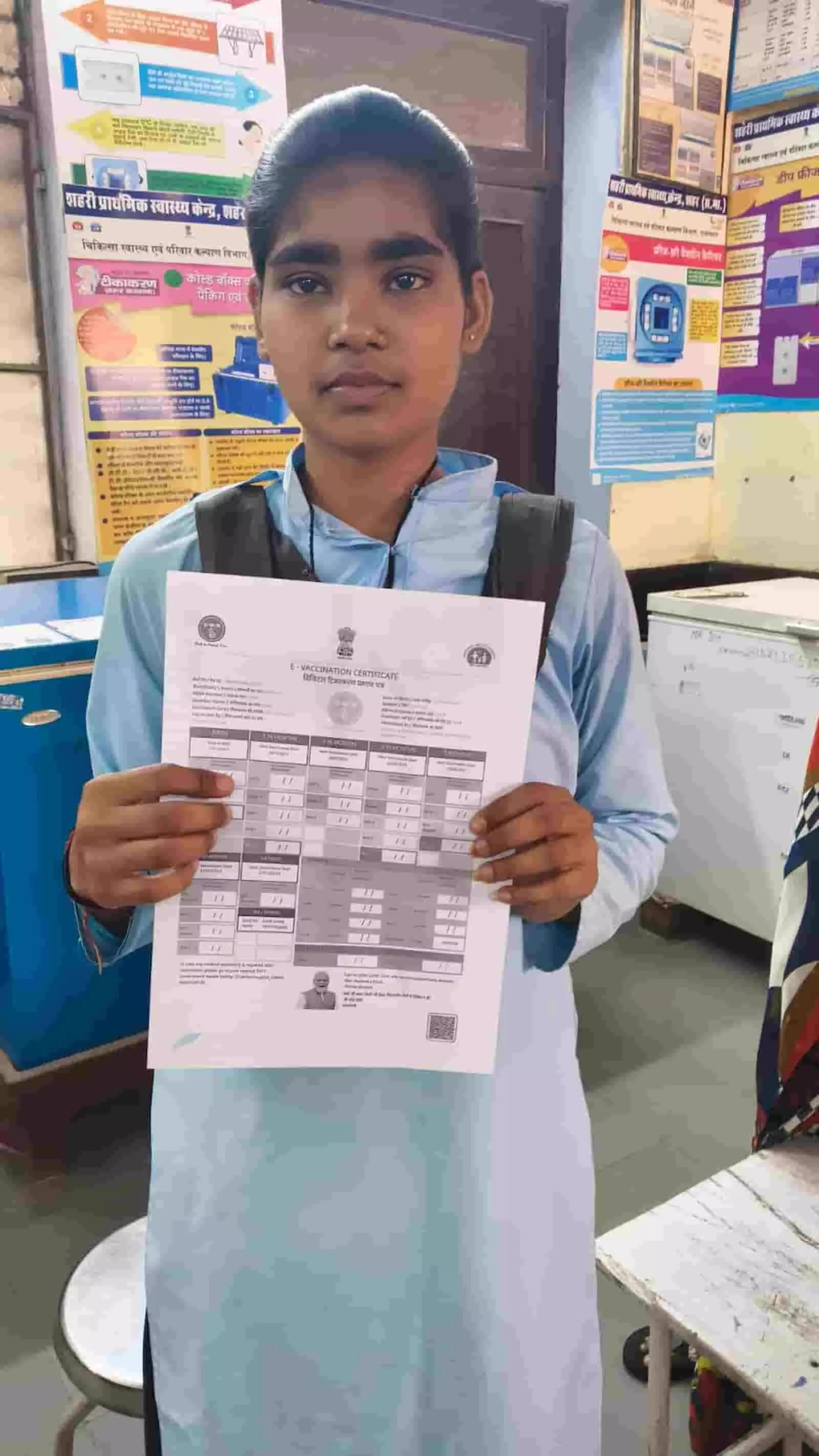 डिस्पेंसरी में खड़ी छात्रा हाथ में अपना ई-वैक्सीनेशन सर्टिफिकेट पकड़कर टीकाकरण का सफल प्रमाण दिखा रही है। डिस्पेंसरी में खड़ी छात्रा हाथ में अपना ई-वैक्सीनेशन सर्टिफिकेट पकड़कर टीकाकरण का सफल प्रमाण दिखा रही है।