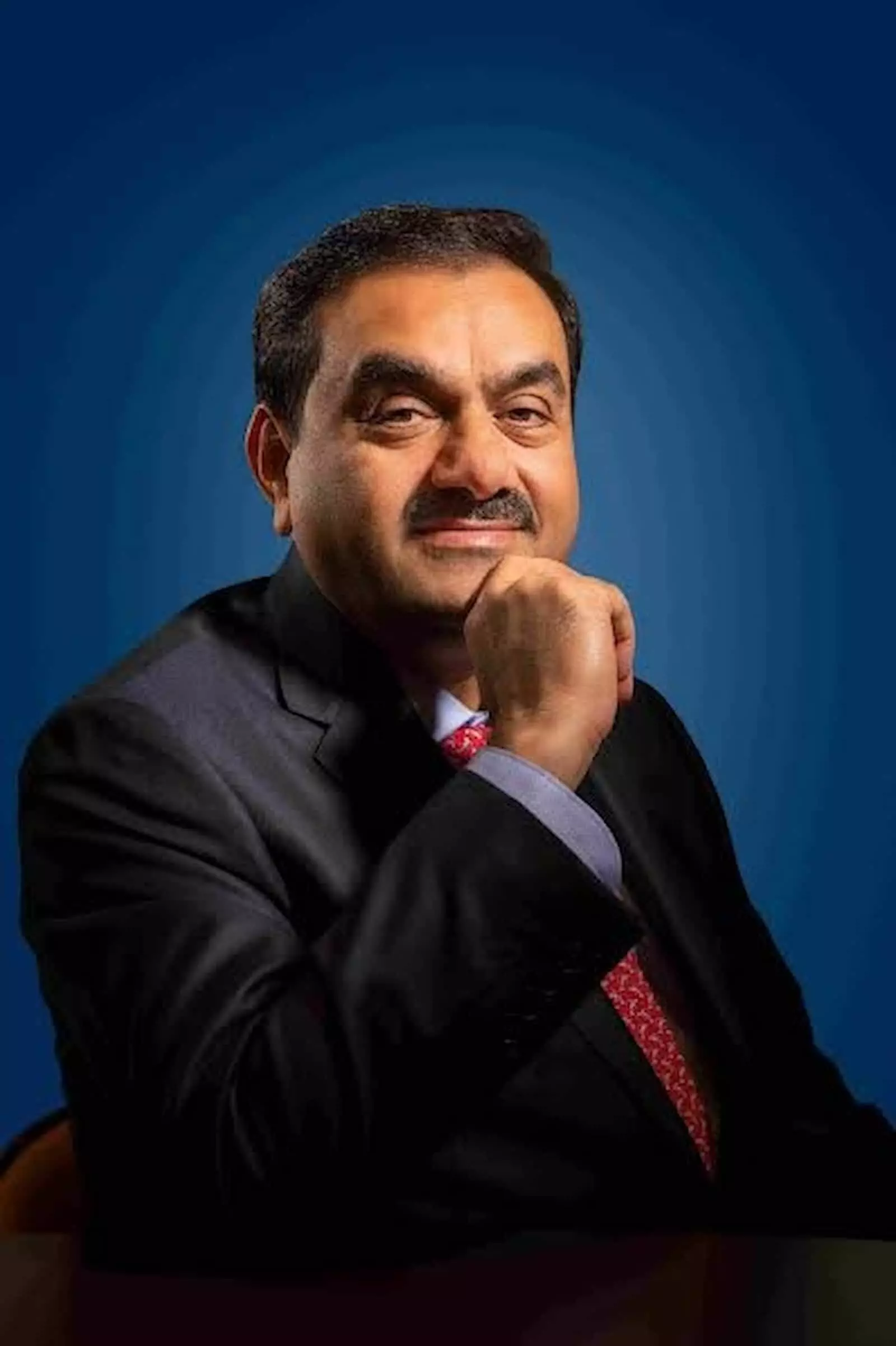 गहरे नीले रंग की पृष्ठभूमि के सामने सूट पहने हुए मुस्कुराते हुए गौतम अदाणी का पोर्ट्रेट। गहरे नीले रंग की पृष्ठभूमि के सामने सूट पहने हुए मुस्कुराते हुए गौतम अदाणी का पोर्ट्रेट।
