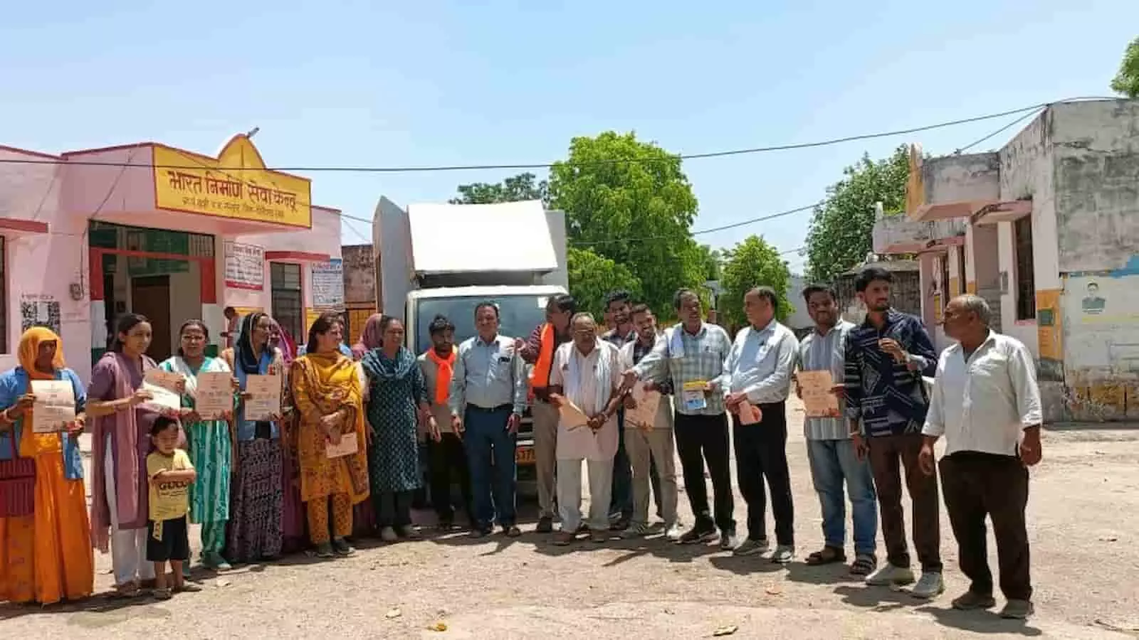 भारत निर्माण सेवा केंद्र के बाहर ग्रामीण और अधिकारी सरकारी योजनाओं के प्रचार रथ के साथ खड़े हैं। भारत निर्माण सेवा केंद्र के बाहर ग्रामीण और अधिकारी सरकारी योजनाओं के प्रचार रथ के साथ खड़े हैं।