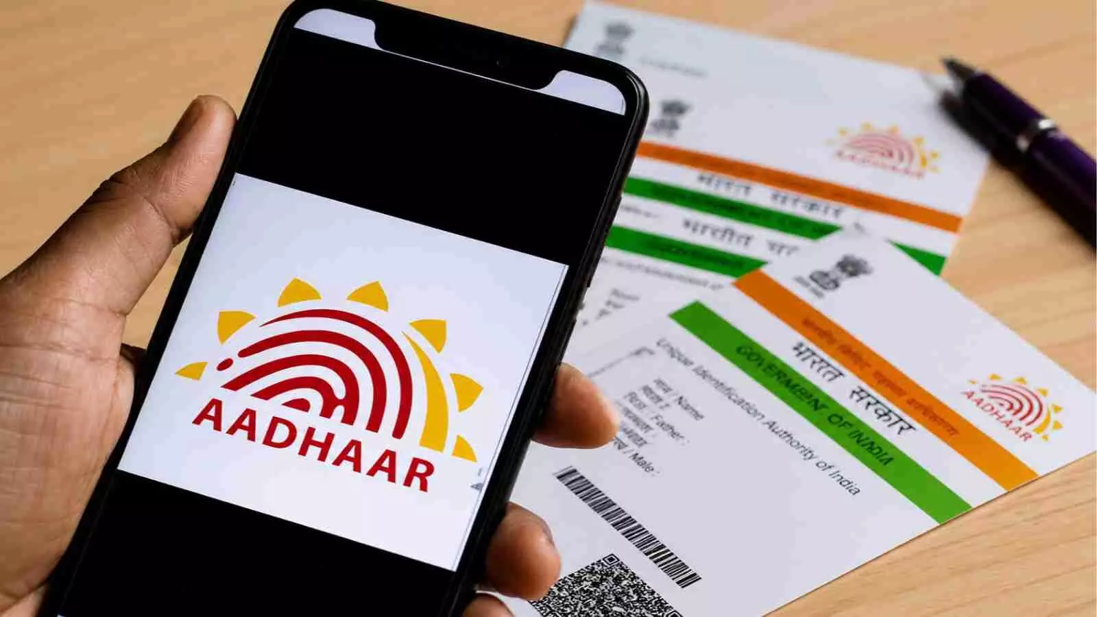 मोबाइल फोन की स्क्रीन पर आधार का लोगो और पास में रखे फिजिकल आधार कार्ड का दृश्य। मोबाइल फोन की स्क्रीन पर आधार का लोगो और पास में रखे फिजिकल आधार कार्ड का दृश्य।