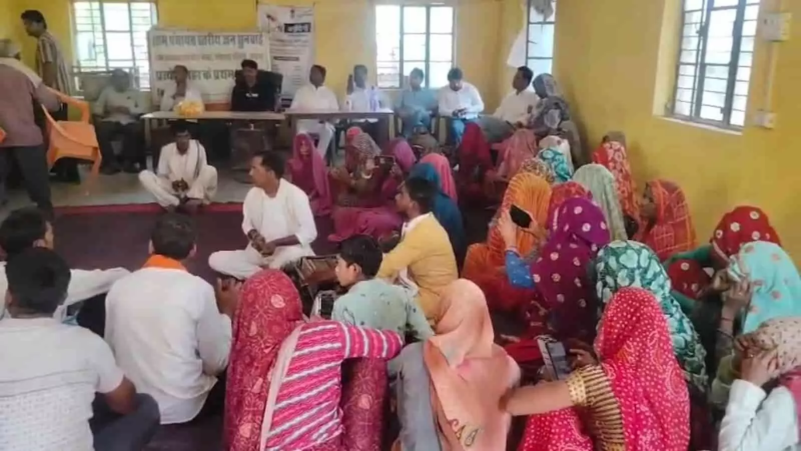 ग्राम पंचायत भवन में दरी पर बैठकर सरकारी योजनाओं की जानकारी सुनते ग्रामीण पुरुष और महिलाएं। ग्राम पंचायत भवन में दरी पर बैठकर सरकारी योजनाओं की जानकारी सुनते ग्रामीण पुरुष और महिलाएं।