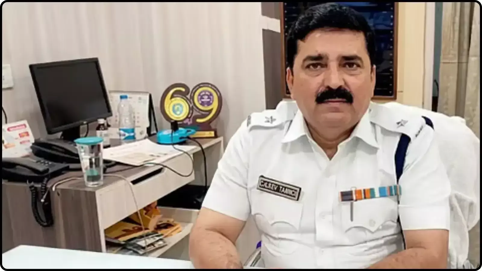 पुलिस की वर्दी पहने अधिकारी शंतनु सिन्हा बिस्वास कार्यालय में मेज के पीछे बैठे हुए दिख रहे हैं। पुलिस की वर्दी पहने अधिकारी शंतनु सिन्हा बिस्वास कार्यालय में मेज के पीछे बैठे हुए दिख रहे हैं।