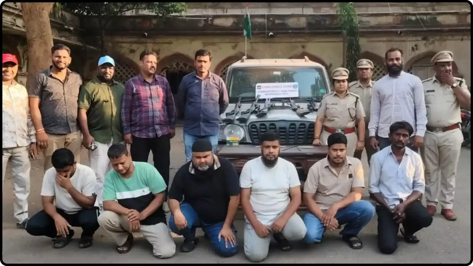 पुलिस अधिकारियों के साथ खड़े और जमीन पर बैठे छह आरोपी और उनके पीछे खड़ी एक स्कॉर्पियो गाड़ी दिख रही है। पुलिस अधिकारियों के साथ खड़े और जमीन पर बैठे छह आरोपी और उनके पीछे खड़ी एक स्कॉर्पियो गाड़ी दिख रही है।