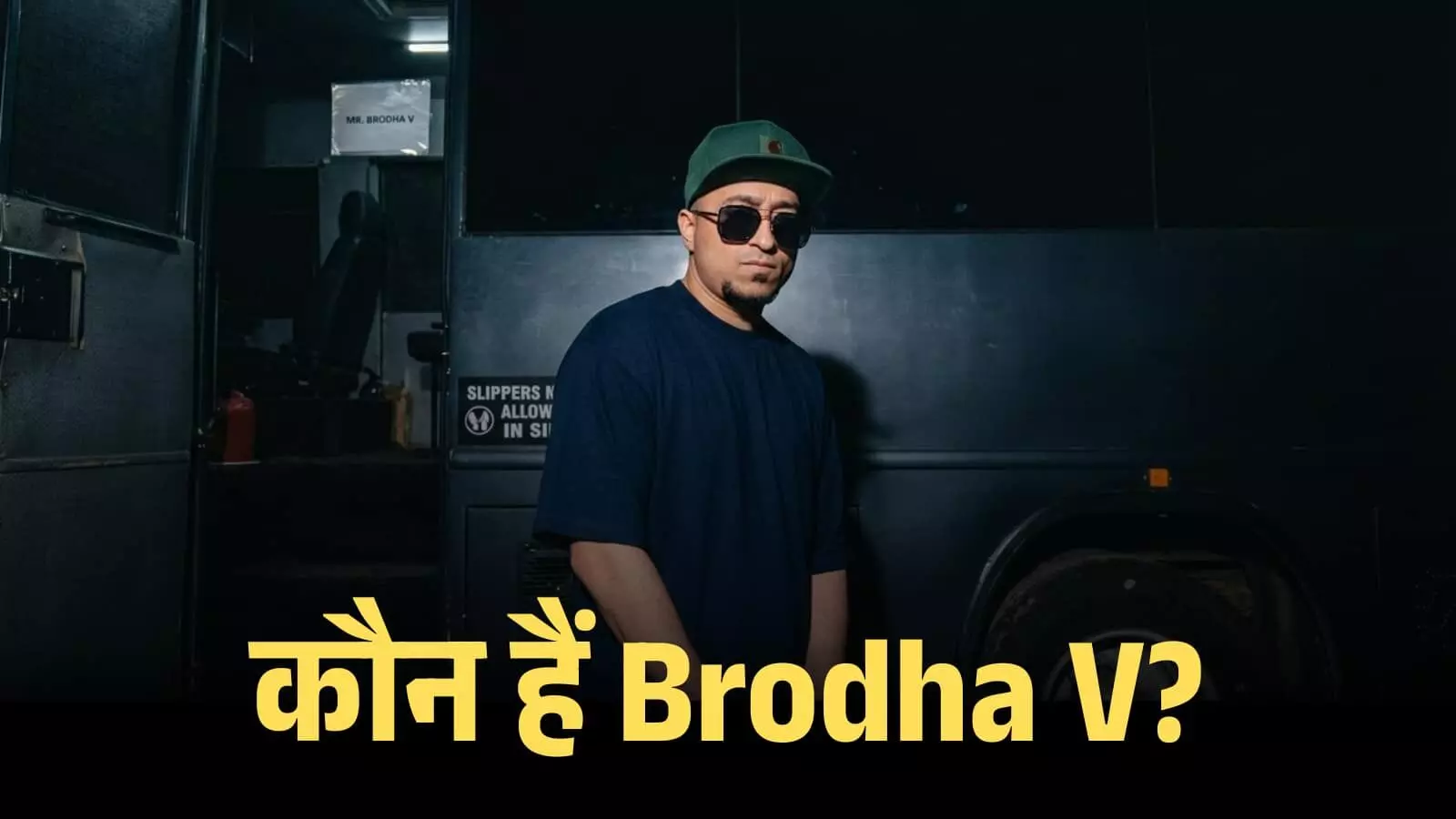 गहरे रंग की टी-शर्ट और टोपी पहने रैपर Brodha V काले रंग की बस के सामने खड़े हैं। गहरे रंग की टी-शर्ट और टोपी पहने रैपर Brodha V काले रंग की बस के सामने खड़े हैं।