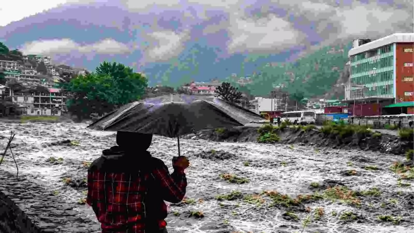 उफनती पहाड़ी नदी और बादलों से ढके पहाड़ के सामने काला छाता लिए खड़ा व्यक्ति। उफनती पहाड़ी नदी और बादलों से ढके पहाड़ के सामने काला छाता लिए खड़ा व्यक्ति।