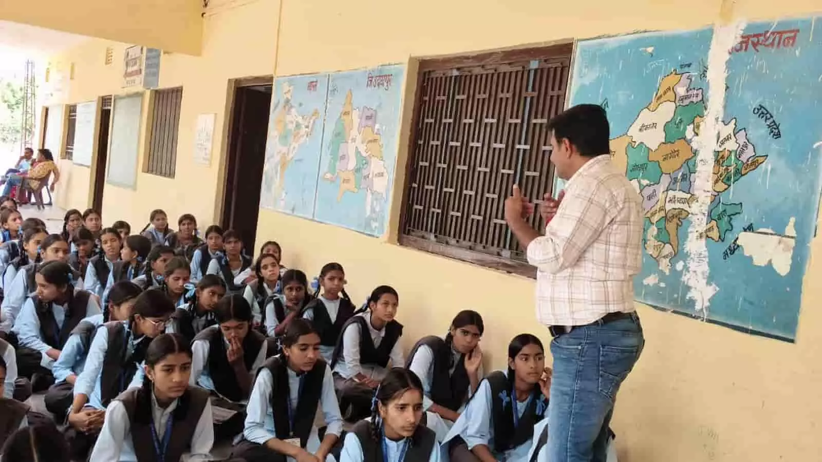 स्कूल परिसर में दीवार पर लगे मानचित्र के पास छात्राओं को संबोधित करते शिक्षक का दृश्य। स्कूल परिसर में दीवार पर लगे मानचित्र के पास छात्राओं को संबोधित करते शिक्षक का दृश्य।