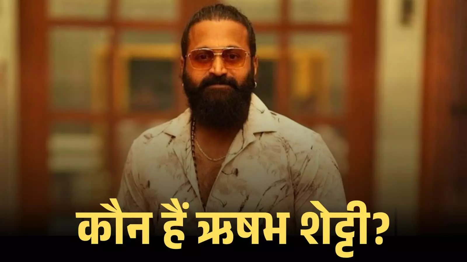 चश्मा और सफेद प्रिंटेड शर्ट पहने हुए अभिनेता ऋषभ शेट्टी एक इंडोर लोकेशन पर खड़े दिख रहे हैं। चश्मा और सफेद प्रिंटेड शर्ट पहने हुए अभिनेता ऋषभ शेट्टी एक इंडोर लोकेशन पर खड़े दिख रहे हैं।