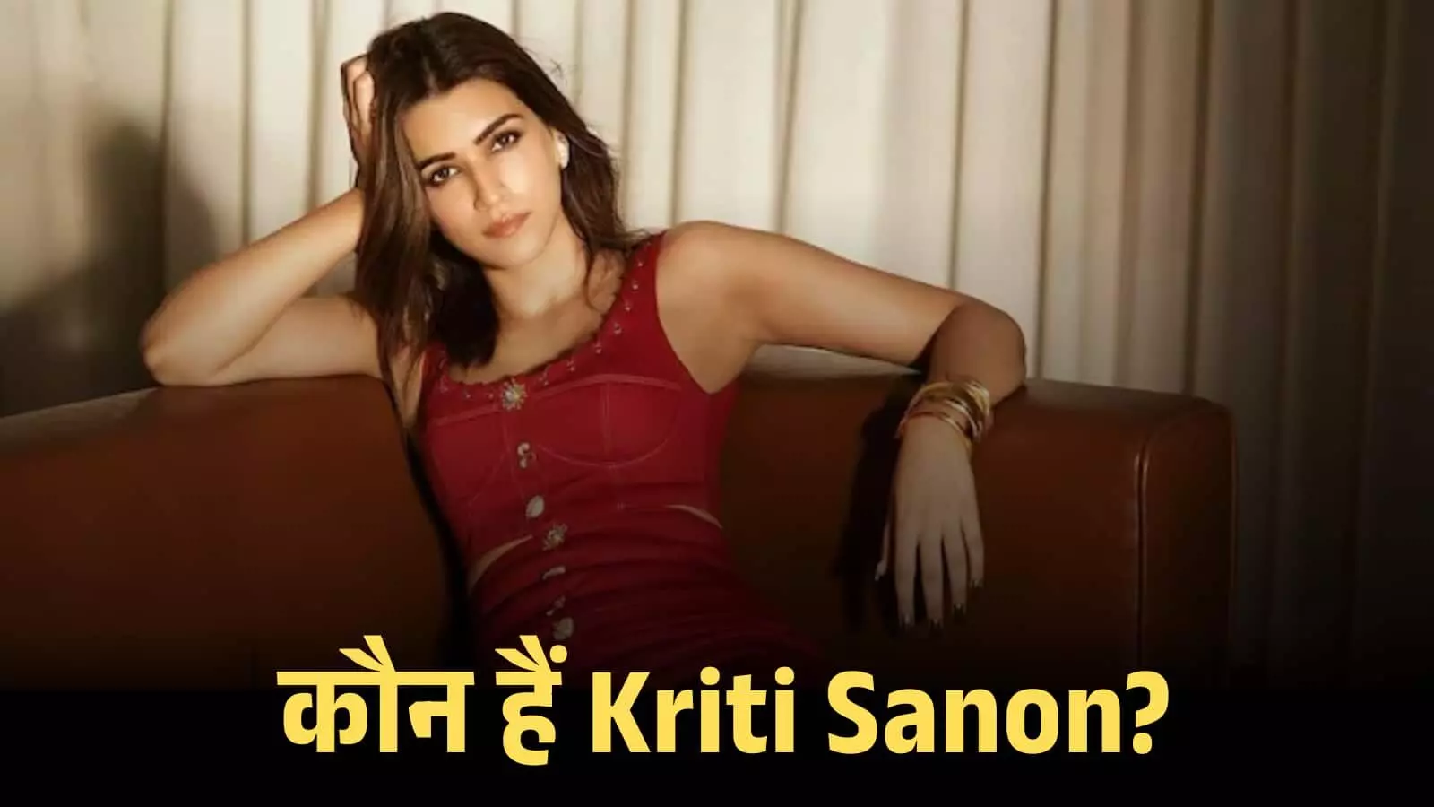 लाल रंग की ड्रेस पहने हुए अभिनेत्री कृति सेनन सोफे पर बैठकर कैमरे की तरफ देख रही हैं।
