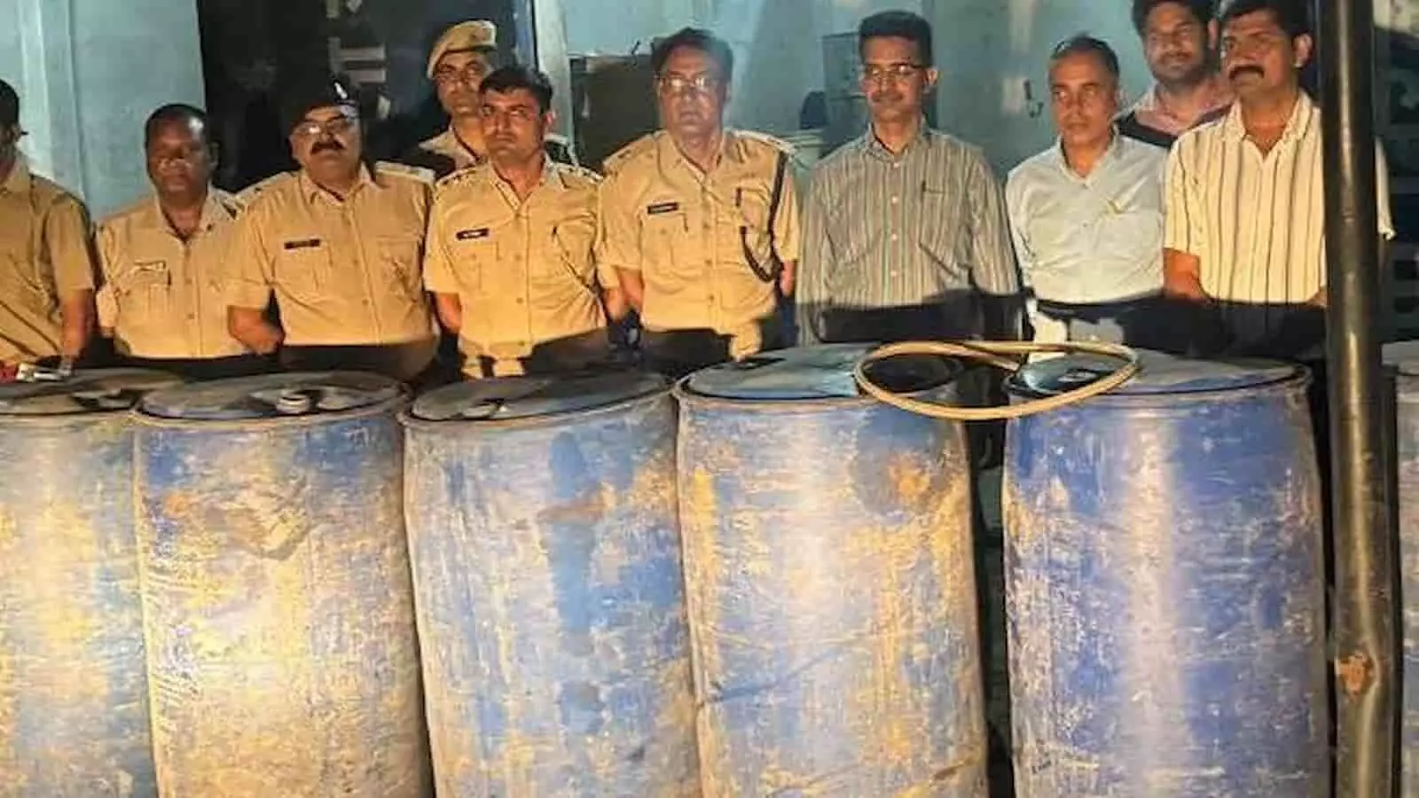 चित्तौड़गढ़ में आबकारी विभाग के अधिकारी जब्त किए गए नीले रंग के स्प्रिट ड्रमों के साथ खड़े हुए।