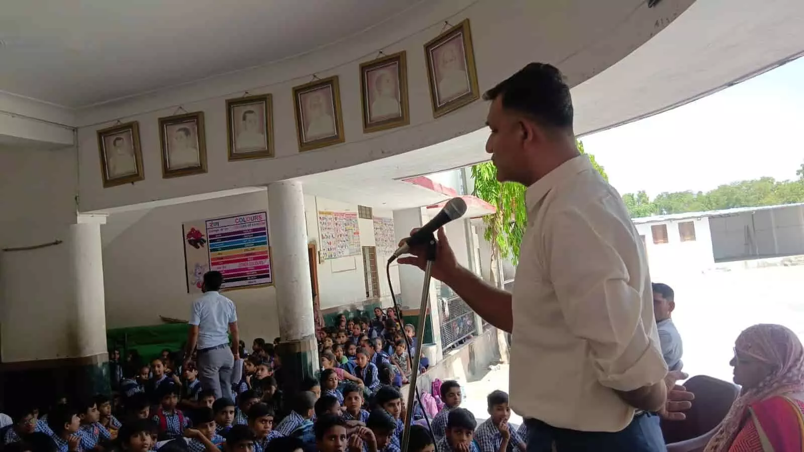 स्कूल परिसर में माइक पर भाषण देते व्यक्ति और सामने बैठे विद्यार्थी महाराणा प्रताप जयंती कार्यक्रम में।