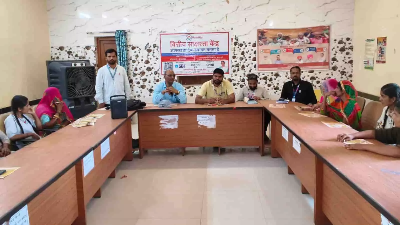 मोहनगढ़ में वित्तीय साक्षरता केंद्र के बैनर तले अधिकारी और ग्रामीण महिलाएं बैंकिंग प्रशिक्षण चर्चा में भाग लेते हुए।