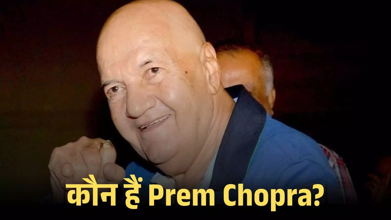 मुस्कुराते हुए अभिनेता प्रेम चोपड़ा एक सार्वजनिक समारोह के दौरान नीली शर्ट में दिखाई दे रहे हैं।