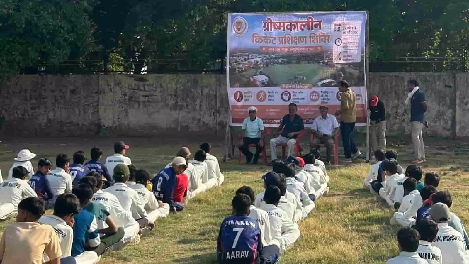 इंद्रा मैदान में ग्रीष्मकालीन क्रिकेट प्रशिक्षण शिविर के समापन पर बैठे हुए अतिथि और सामने जमीन पर बैठे खिलाड़ी।
