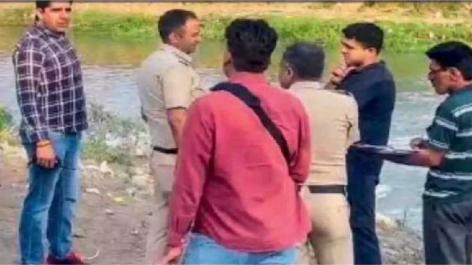 वर्दी में पुलिस अधिकारी और सादे कपड़ों में कुछ लोग नहर के किनारे खड़े होकर बात कर रहे हैं।