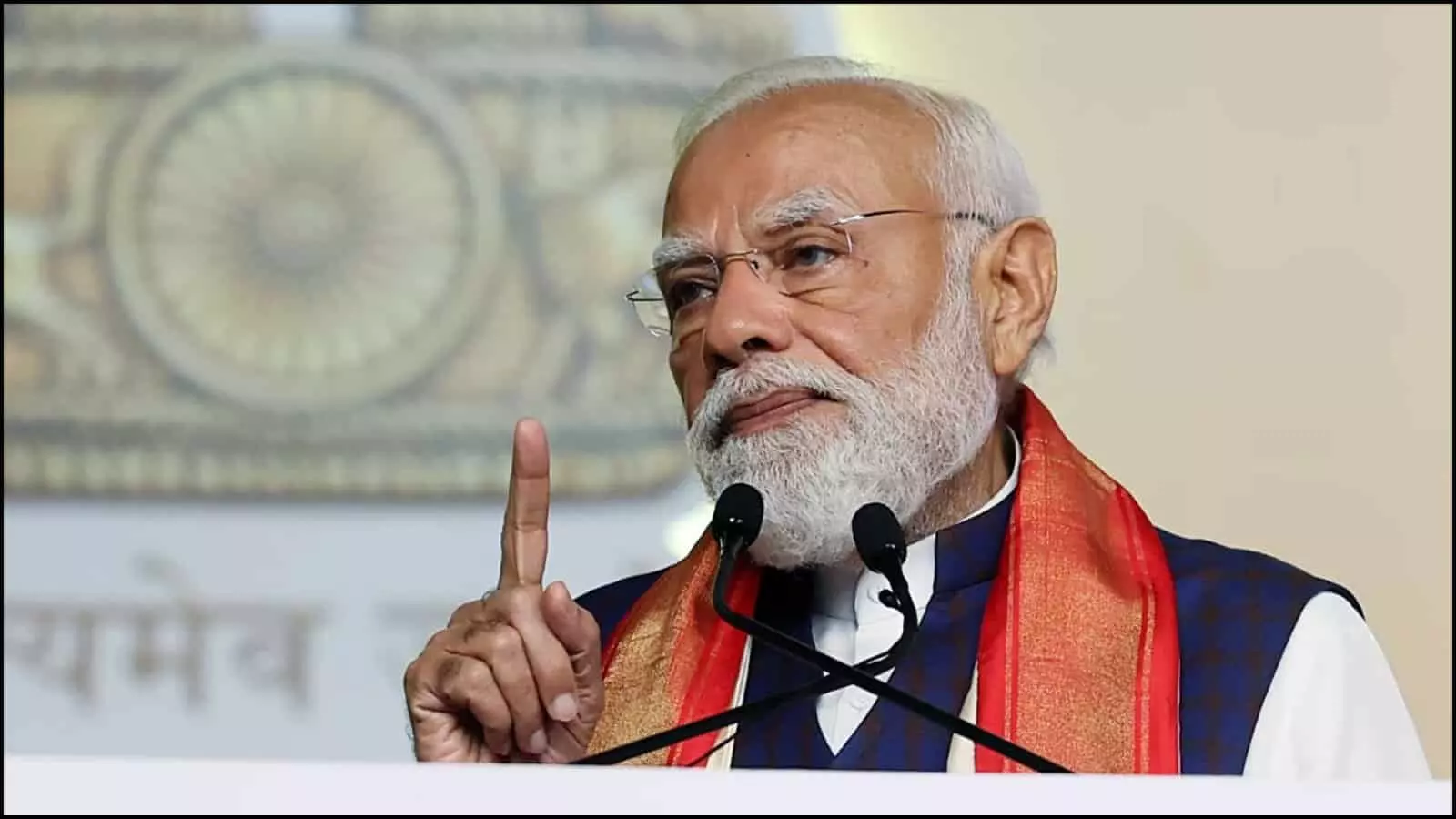 पोडियम पर लगे माइक के सामने हाथ के इशारे से संबोधित करते प्रधानमंत्री नरेंद्र मोदी।