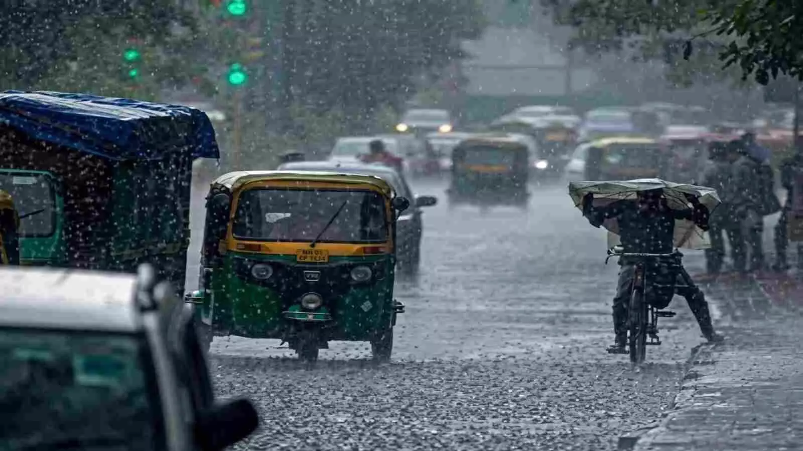 बारिश में सड़क पर चलते ऑटो रिक्शा और छाता लेकर साइकिल चलाता व्यक्ति। बारिश में सड़क पर चलते ऑटो रिक्शा और छाता लेकर साइकिल चलाता व्यक्ति।