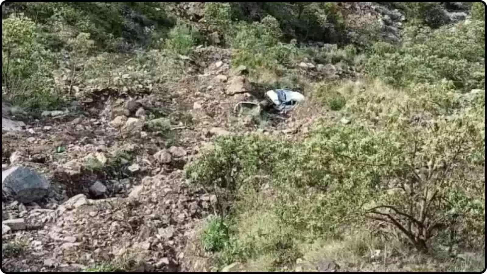 गहरी पथरीली खाई और झाड़ियों के बीच दुर्घटनाग्रस्त सफेद रंग की गाड़ी का मलबा।