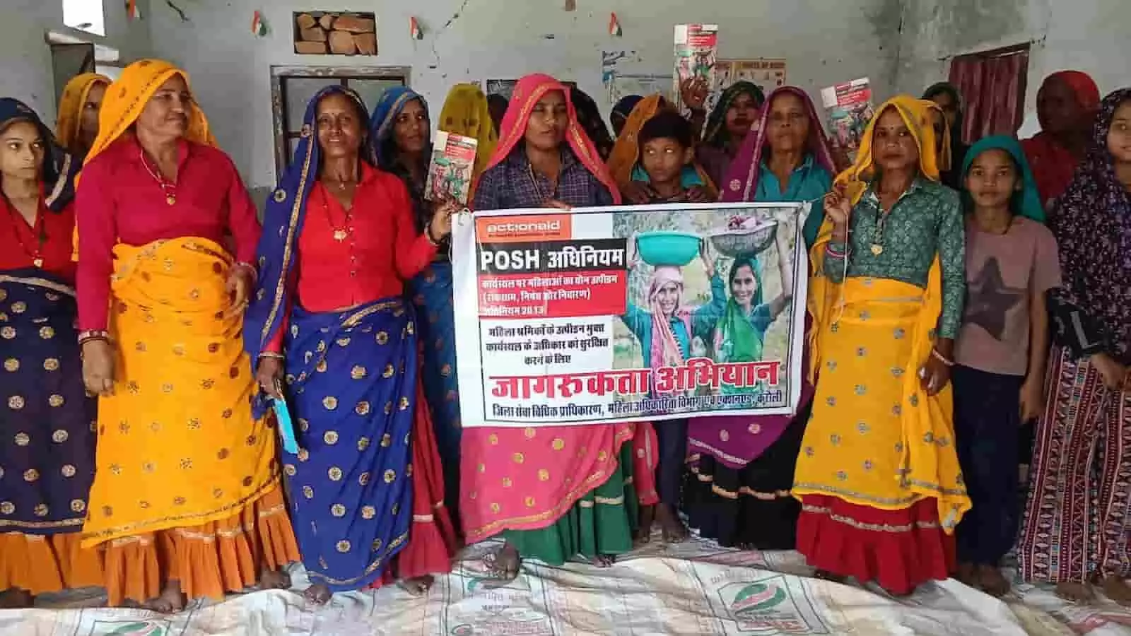 सपोटरा के रूपपुरा में POSH अधिनियम जागरूकता बैनर के साथ खड़ी महिला श्रमिक और समुदाय के लोग।