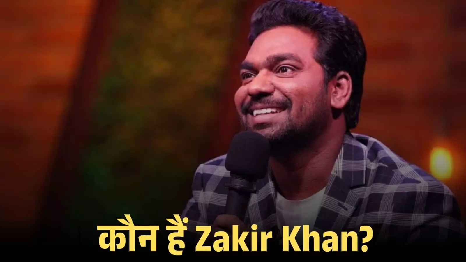 स्टैंडअप कॉमेडियन जाकिर खान हाथ में माइक थामे हुए मंच पर कॉमेडी शो के दौरान हंसते हुए।