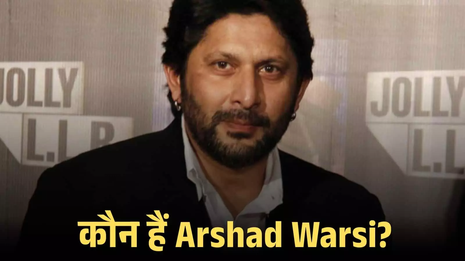 बॉलीवुड अभिनेता अरशद वारसी एक फिल्म प्रमोशन कार्यक्रम के दौरान काले कोट में मुस्कुराते हुए।