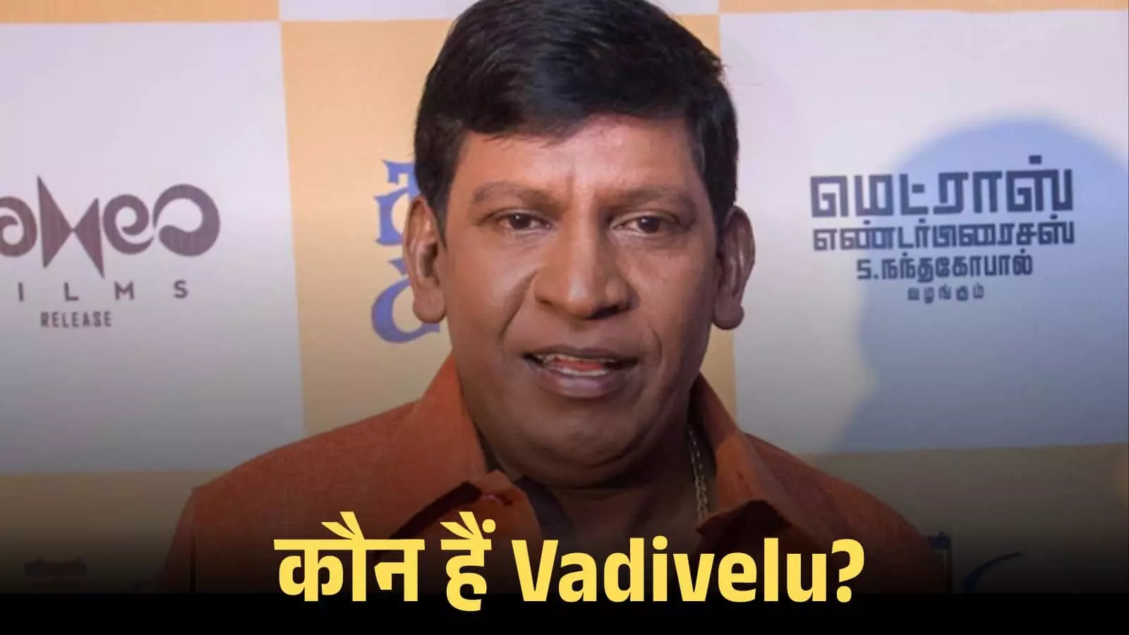 कैमरे के सामने सीधे देख रहे अभिनेता वडिवेलु एक प्रेस कॉन्फ्रेंस के दौरान नारंगी शर्ट पहने हुए। कैमरे के सामने सीधे देख रहे अभिनेता वडिवेलु एक प्रेस कॉन्फ्रेंस के दौरान नारंगी शर्ट पहने हुए।