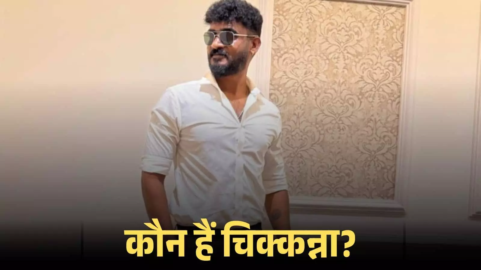 चश्मा और सफेद शर्ट पहने अभिनेता चिक्कन्ना एक सजावटी दीवार के सामने खड़े होकर पोज दे रहे हैं। चश्मा और सफेद शर्ट पहने अभिनेता चिक्कन्ना एक सजावटी दीवार के सामने खड़े होकर पोज दे रहे हैं।