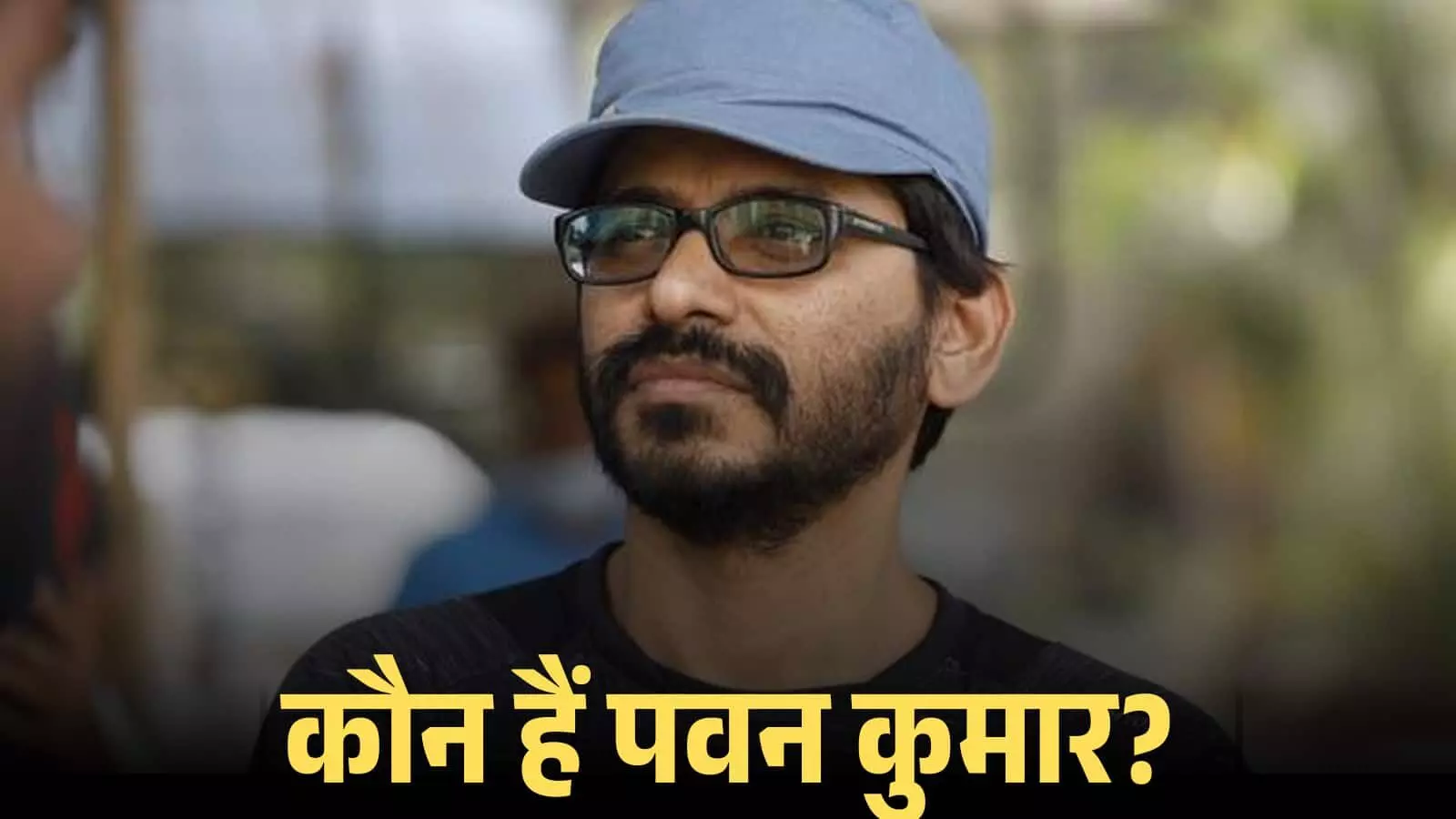 चश्मा और नीली टोपी पहने हुए निर्देशक पवन कुमार एक फिल्म सेट के दौरान बाहर देख रहे हैं। चश्मा और नीली टोपी पहने हुए निर्देशक पवन कुमार एक फिल्म सेट के दौरान बाहर देख रहे हैं।