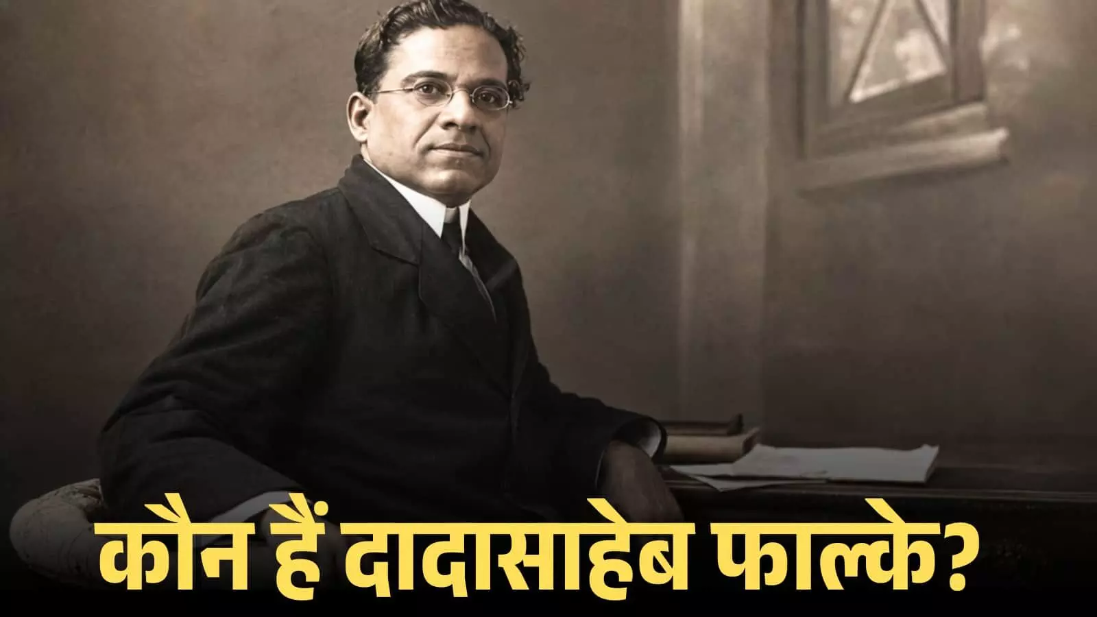 चश्मा और सूट पहने हुए दादासाहेब फाल्के एक मेज के पास बैठकर कैमरा की ओर देख रहे हैं। चश्मा और सूट पहने हुए दादासाहेब फाल्के एक मेज के पास बैठकर कैमरा की ओर देख रहे हैं।