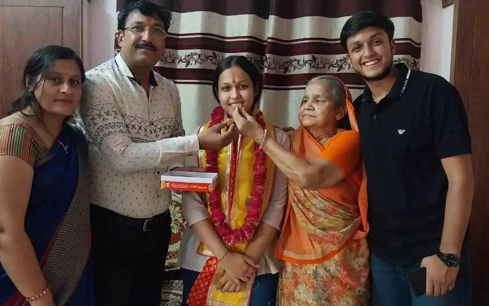 माला पहने खड़ी छात्रा को मिठाई खिलाते परिजन चित्तौड़गढ़ में बोर्ड परीक्षा परिणाम का उत्सव मना रहे हैं। माला पहने खड़ी छात्रा को मिठाई खिलाते परिजन चित्तौड़गढ़ में बोर्ड परीक्षा परिणाम का उत्सव मना रहे हैं।