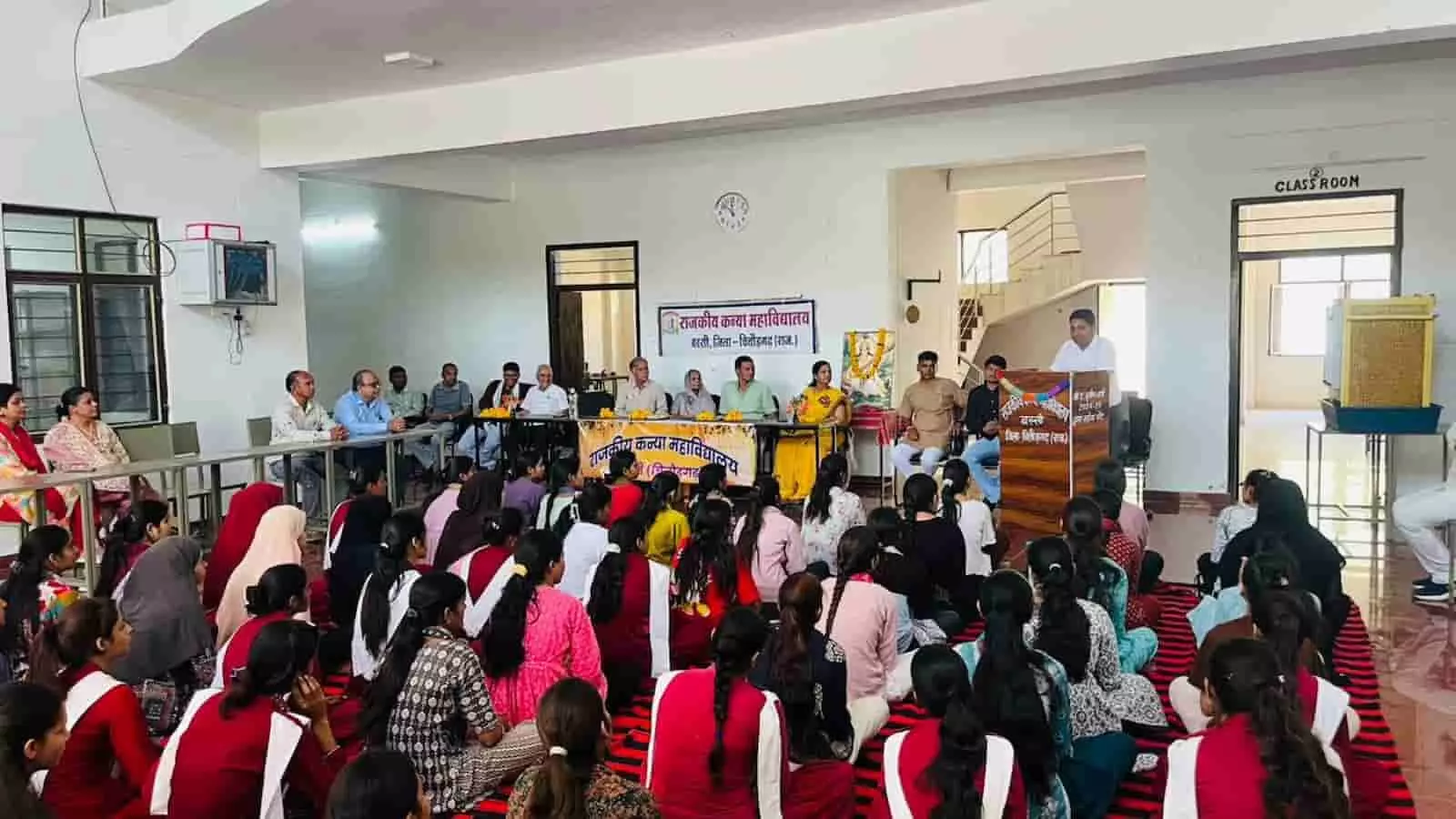 महाविद्यालय के हॉल में मंच पर बैठे अतिथि और नीचे बैठी छात्राओं का समूह कार्यक्रम के दौरान। महाविद्यालय के हॉल में मंच पर बैठे अतिथि और नीचे बैठी छात्राओं का समूह कार्यक्रम के दौरान।