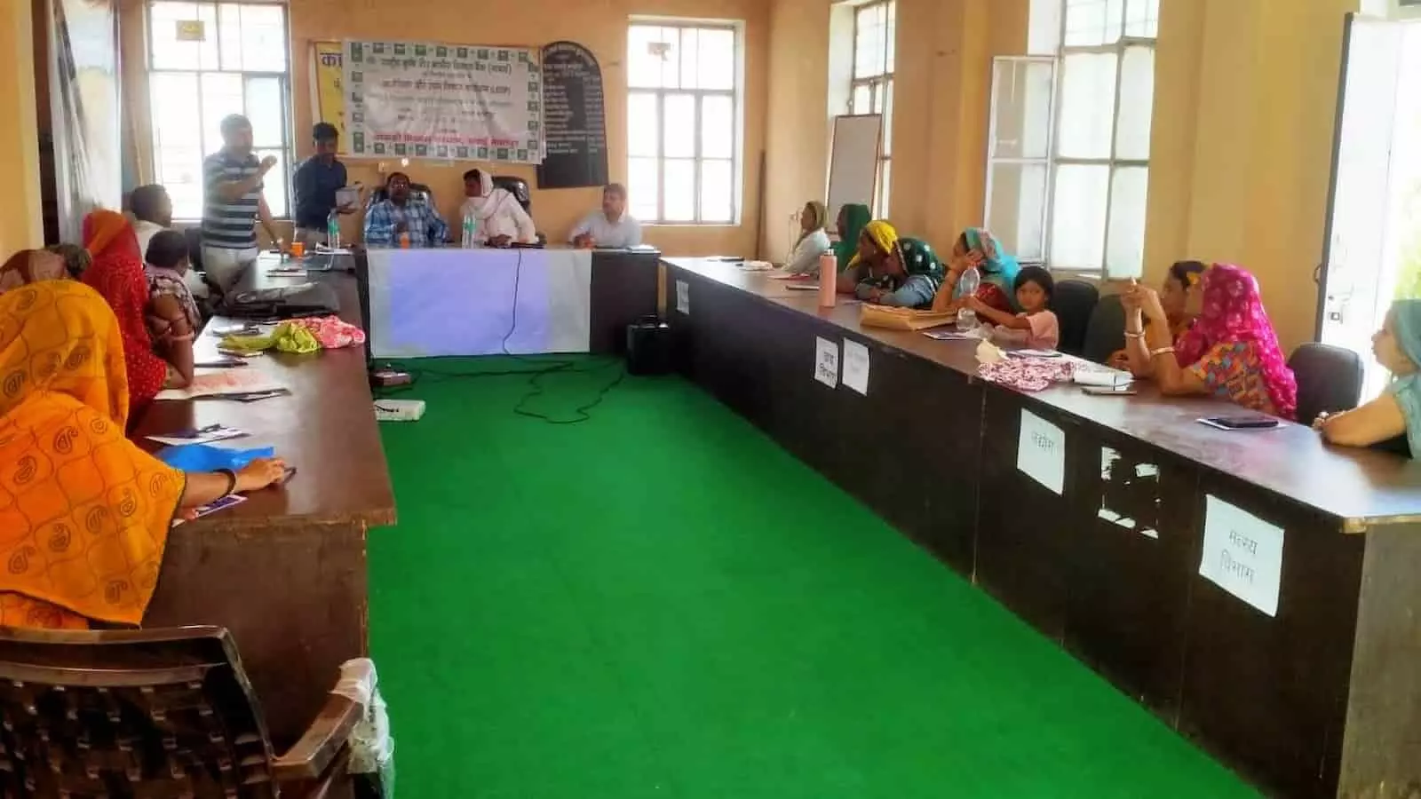 कुस्तला में प्रशिक्षण सत्र के दौरान मेज के चारों ओर बैठी स्वयं सहायता समूह की महिलाएं और प्रशिक्षण देते अधिकारी।