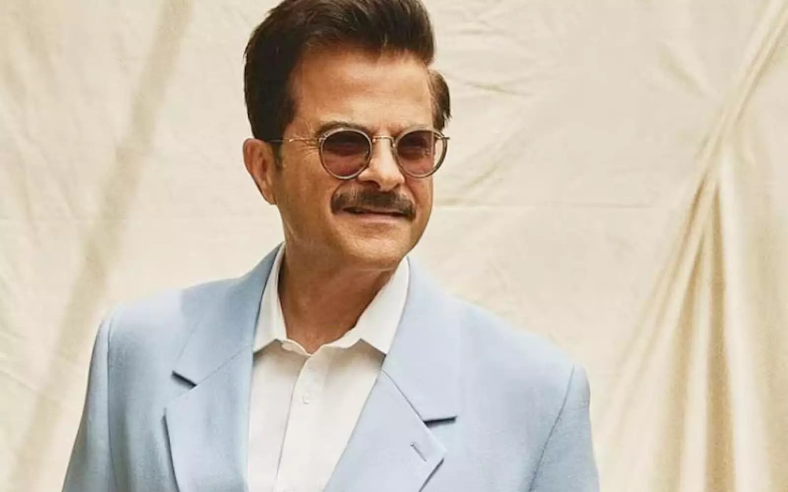 नीले रंग के कोट में मुस्कुराते हुए अभिनेता अनिल कपूर एक इवेंट के दौरान पोज़ देते हुए।