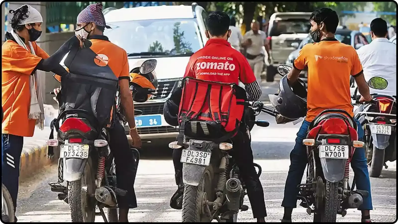 सड़क पर खड़े होकर मोटरसाइकिल पर बैठे जोमैटो और शैडोफैक्स कंपनी के तीन डिलीवरी पार्टनर्स। सड़क पर खड़े होकर मोटरसाइकिल पर बैठे जोमैटो और शैडोफैक्स कंपनी के तीन डिलीवरी पार्टनर्स।