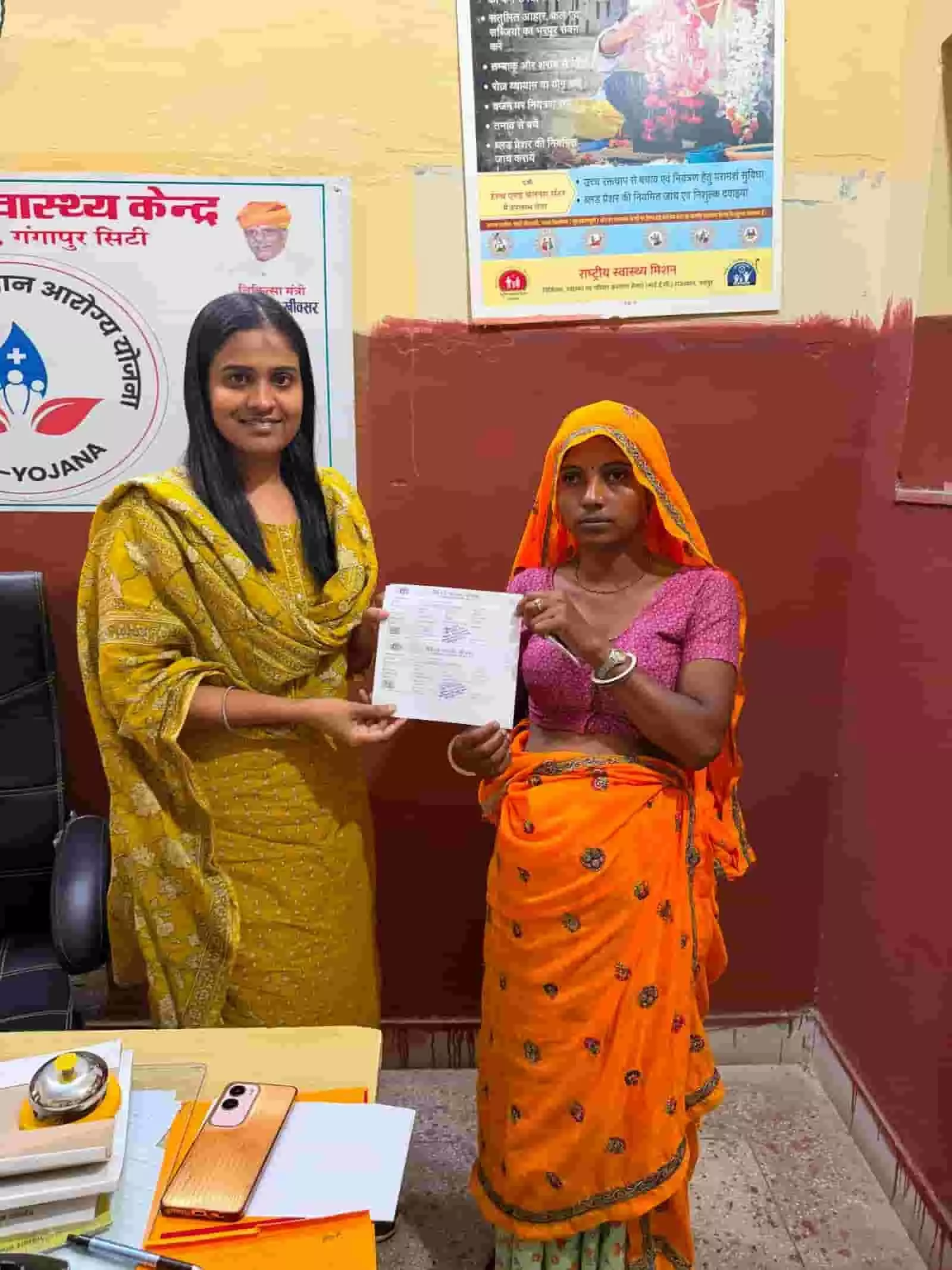 गंगापुर सिटी स्वास्थ्य केंद्र में चिकित्सा अधिकारी से जांच पर्ची और मां वाउचर लेती हुई एक ग्रामीण गर्भवती महिला।