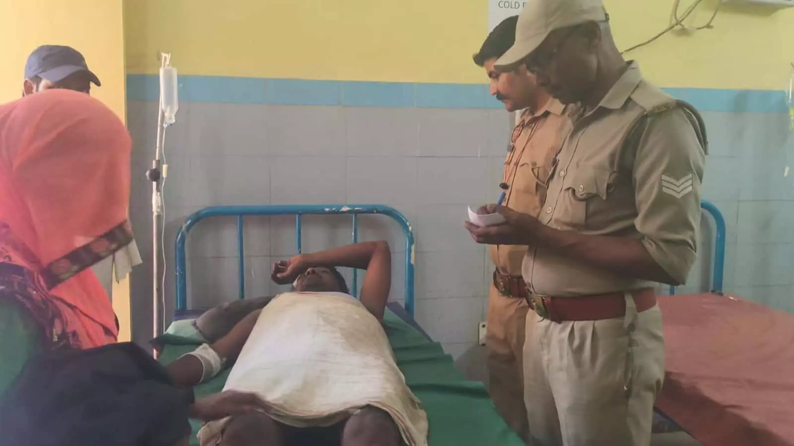 अस्पताल के बिस्तर पर लेटा घायल व्यक्ति और पास खड़े पुलिसकर्मी सड़क हादसे की जांच करते हुए। अस्पताल के बिस्तर पर लेटा घायल व्यक्ति और पास खड़े पुलिसकर्मी सड़क हादसे की जांच करते हुए।