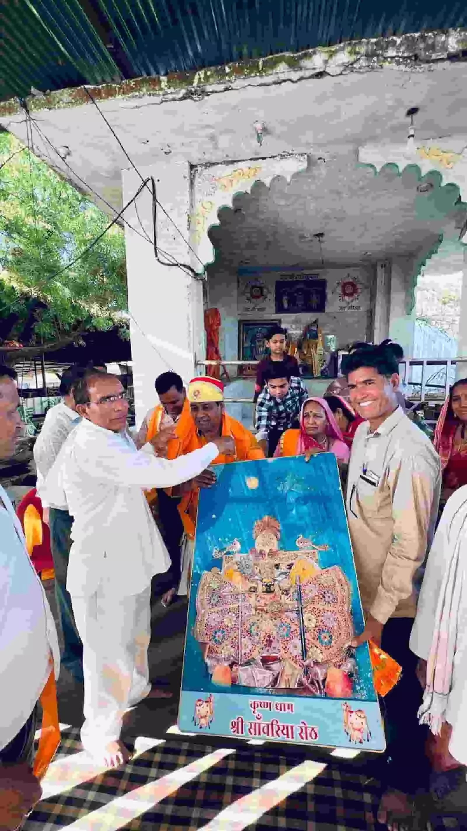 भिंडर के गौशाला प्रांगण में हाथ में भगवान श्रीकृष्ण की तस्वीर पकड़े हुए खड़े ग्रामीण पुरुष और महिलाएं। भिंडर के गौशाला प्रांगण में हाथ में भगवान श्रीकृष्ण की तस्वीर पकड़े हुए खड़े ग्रामीण पुरुष और महिलाएं।
