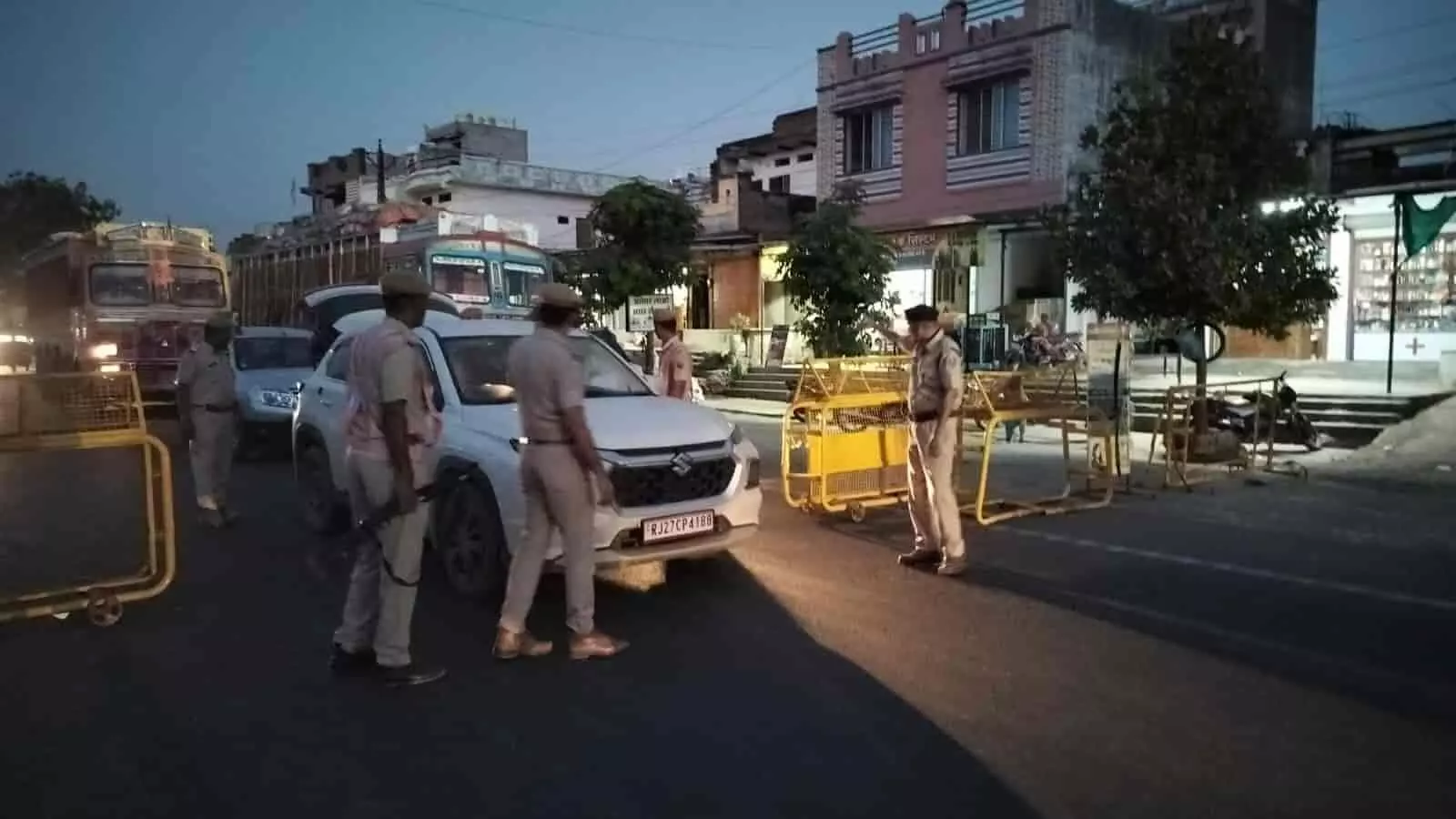सड़क पर खड़ी सफेद रंग की गाड़ी के पास जांच करते राजस्थान पुलिस के जवान नाकाबंदी के दौरान।