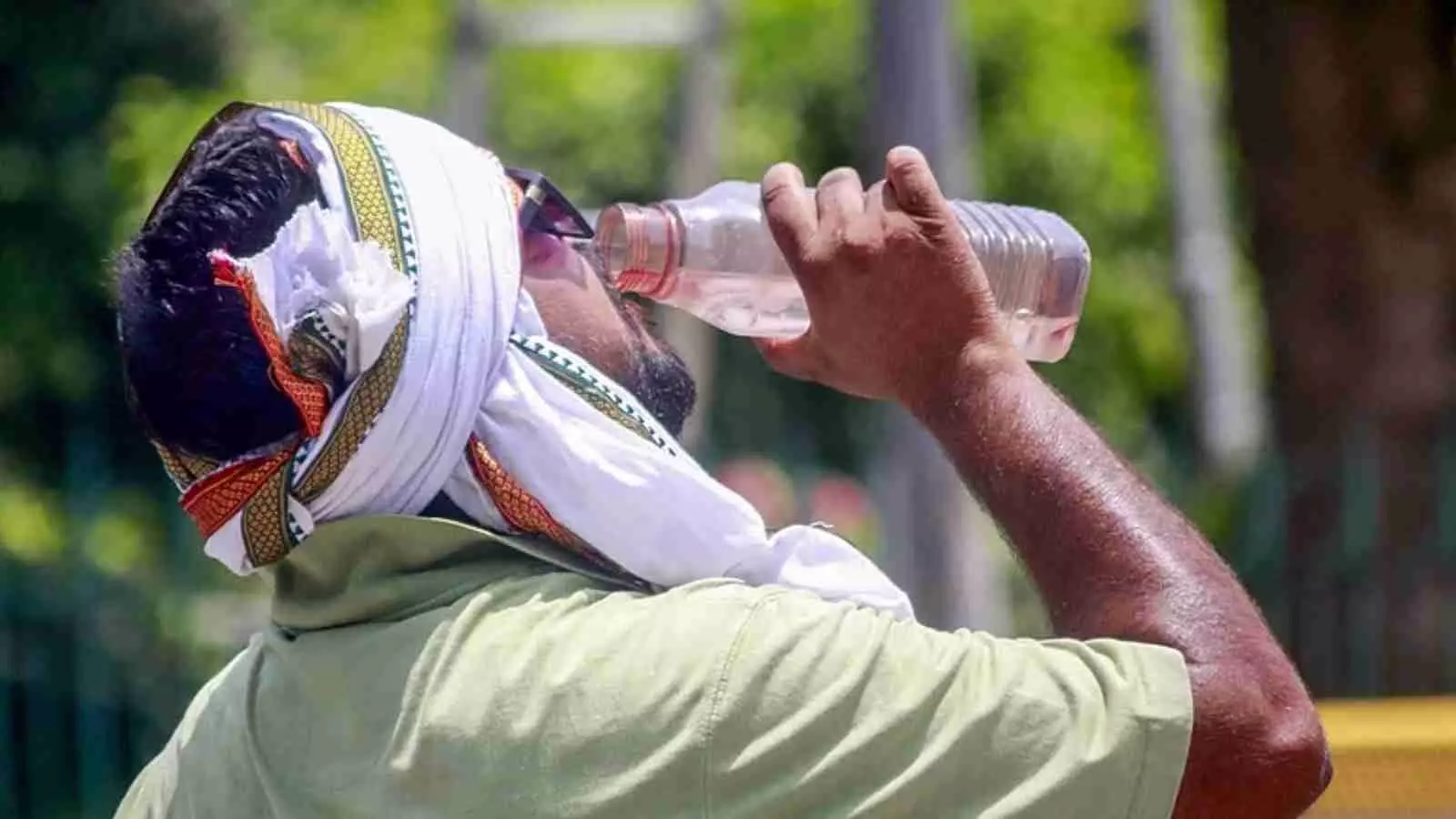 सिर पर कपड़ा बांधकर बोतल से पानी पीता हुआ व्यक्ति धूप और गर्मी के संदर्भ में। सिर पर कपड़ा बांधकर बोतल से पानी पीता हुआ व्यक्ति धूप और गर्मी के संदर्भ में।