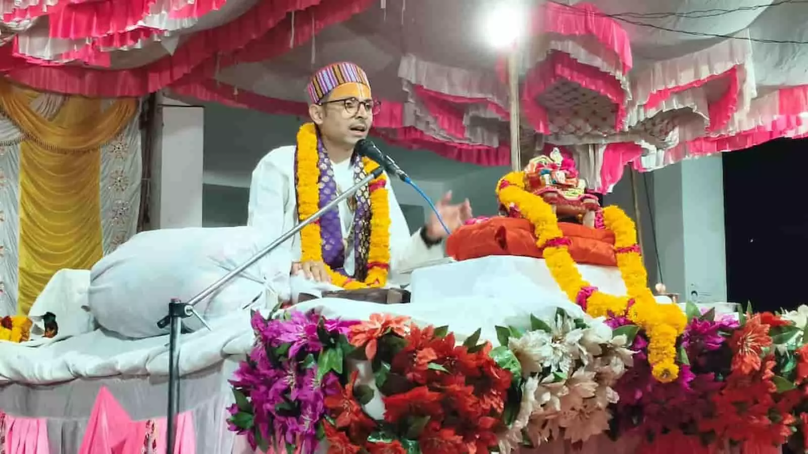 आमेट के हनुमान मंदिर में मंच पर बैठकर माइक के सामने प्रवचन देते कथाव्यास श्री युवराज कृष्ण महाराज।