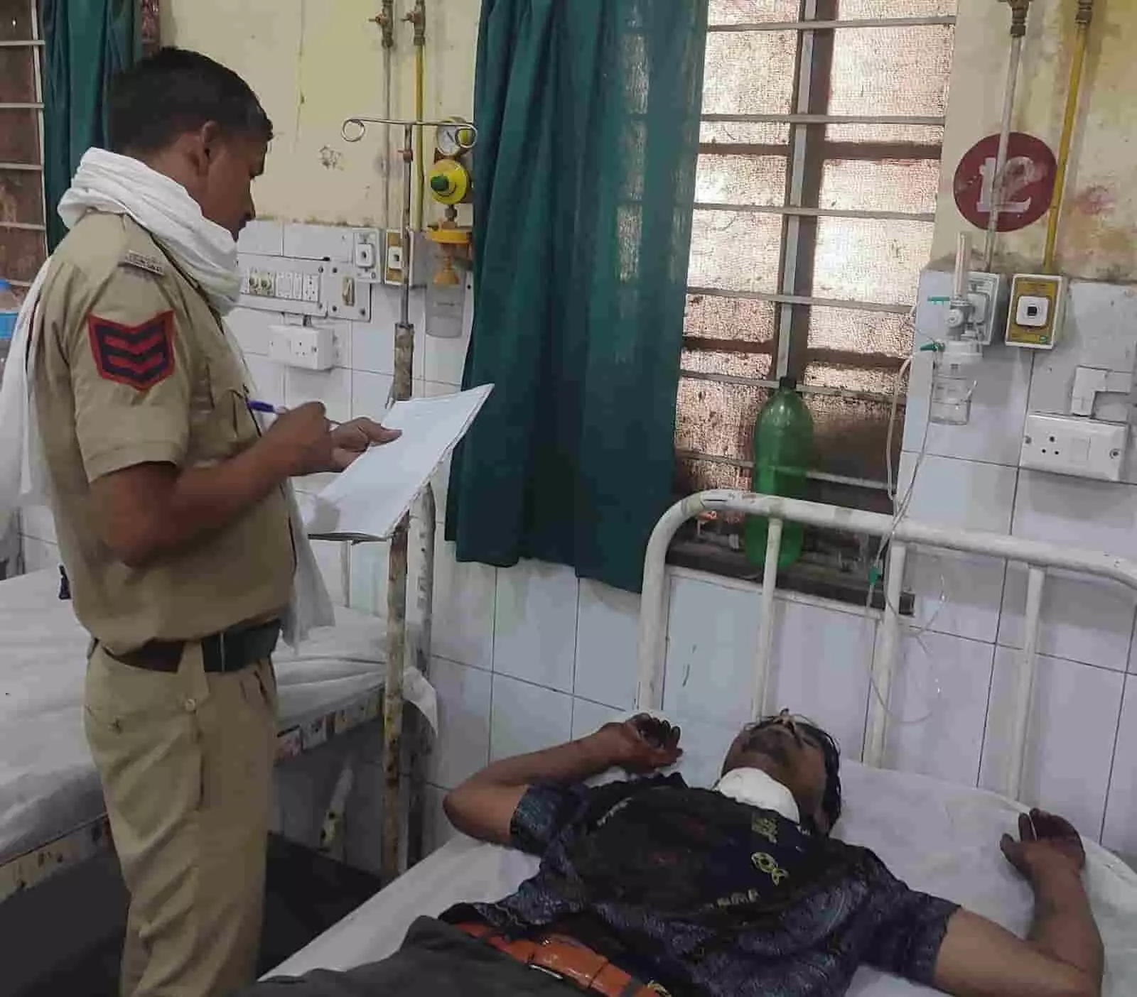 अस्पताल के बेड पर घायल व्यक्ति और पूछताछ करता हुआ पुलिसकर्मी अस्पताल के बेड पर घायल व्यक्ति और पूछताछ करता हुआ पुलिसकर्मी